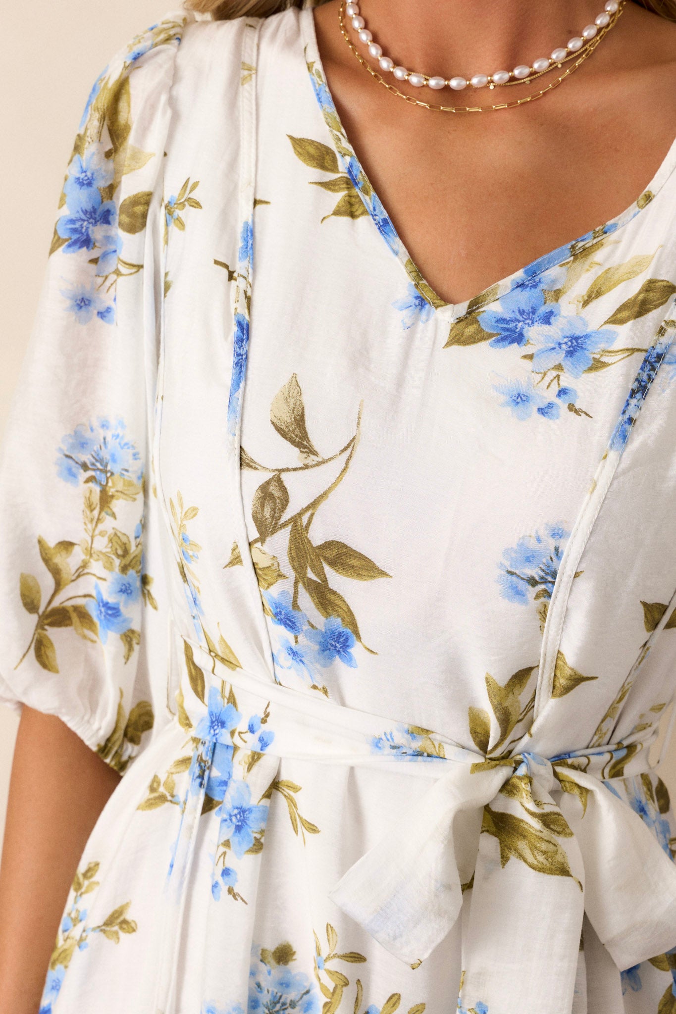 Close-up of this blue & white floral dress, highlighting the V-neckline, puff sleeves, and tied waist detail.