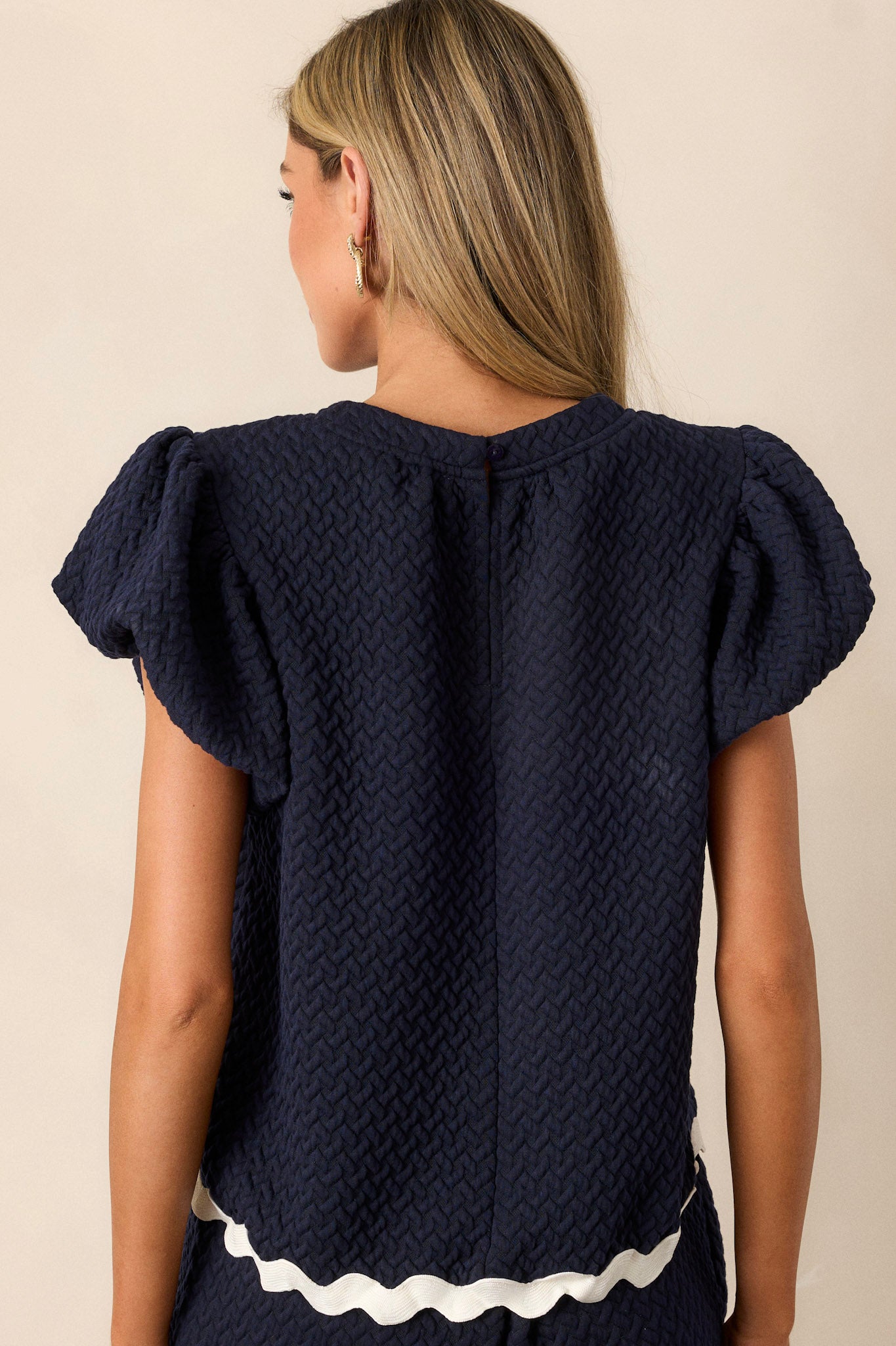 Back view of a navy top highlighting the overall fit, quilted material, and contrasting scalloped hemline.