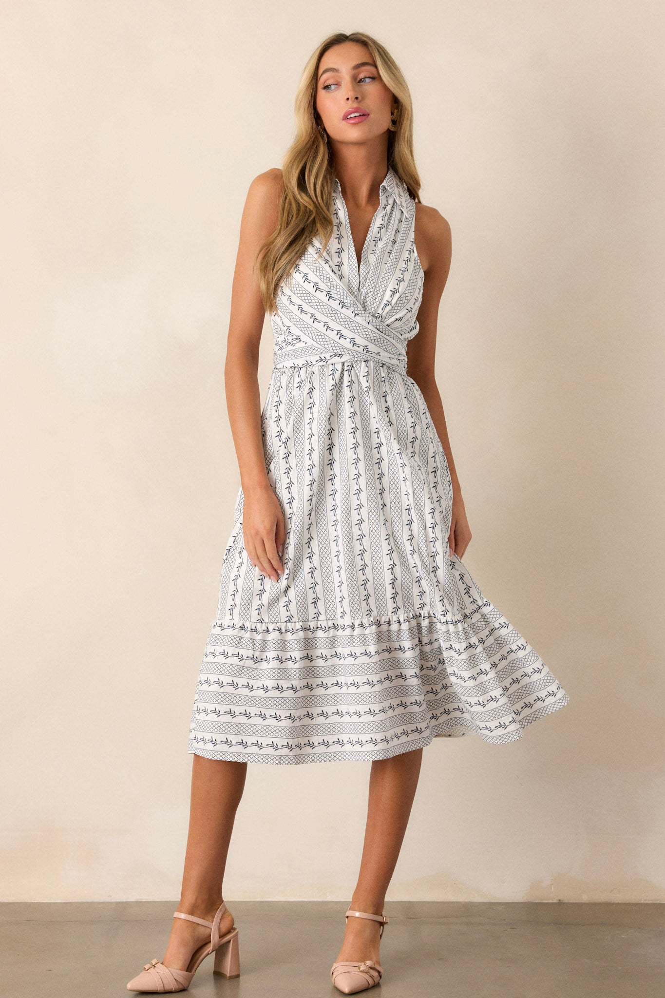 This ivory dress features navy blue floral print, a collared neckline, a self tie detail, and a ruffled bottom edge.