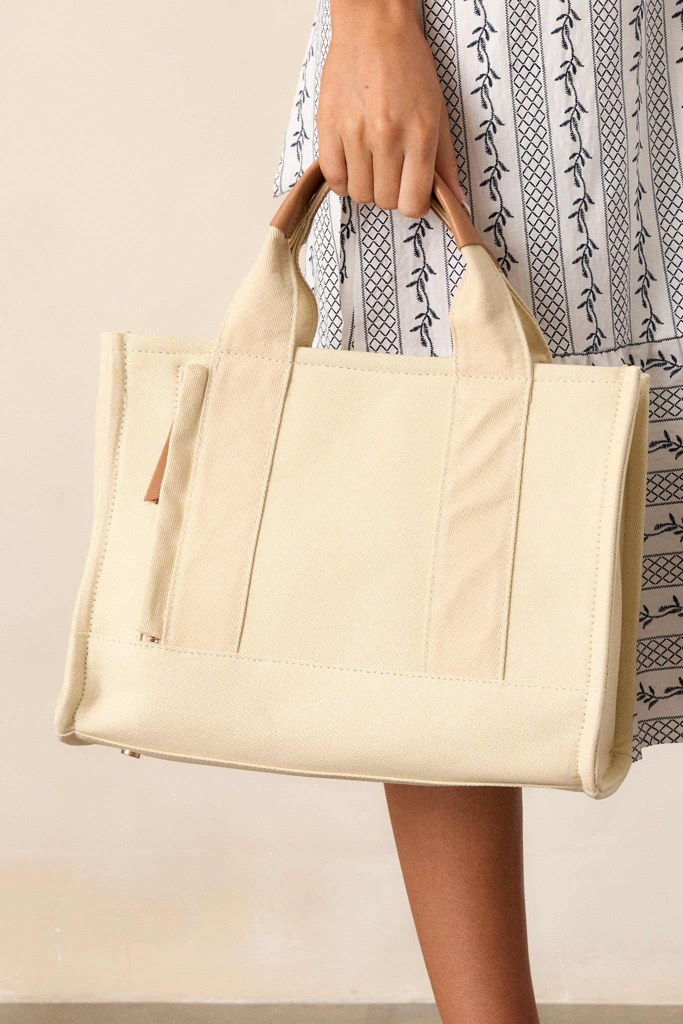 Close-up view of this canvas bag featuring gold hardware, top handles, a functional zipper closure, an additional pocket on the inside, and a removable strap.&nbsp;