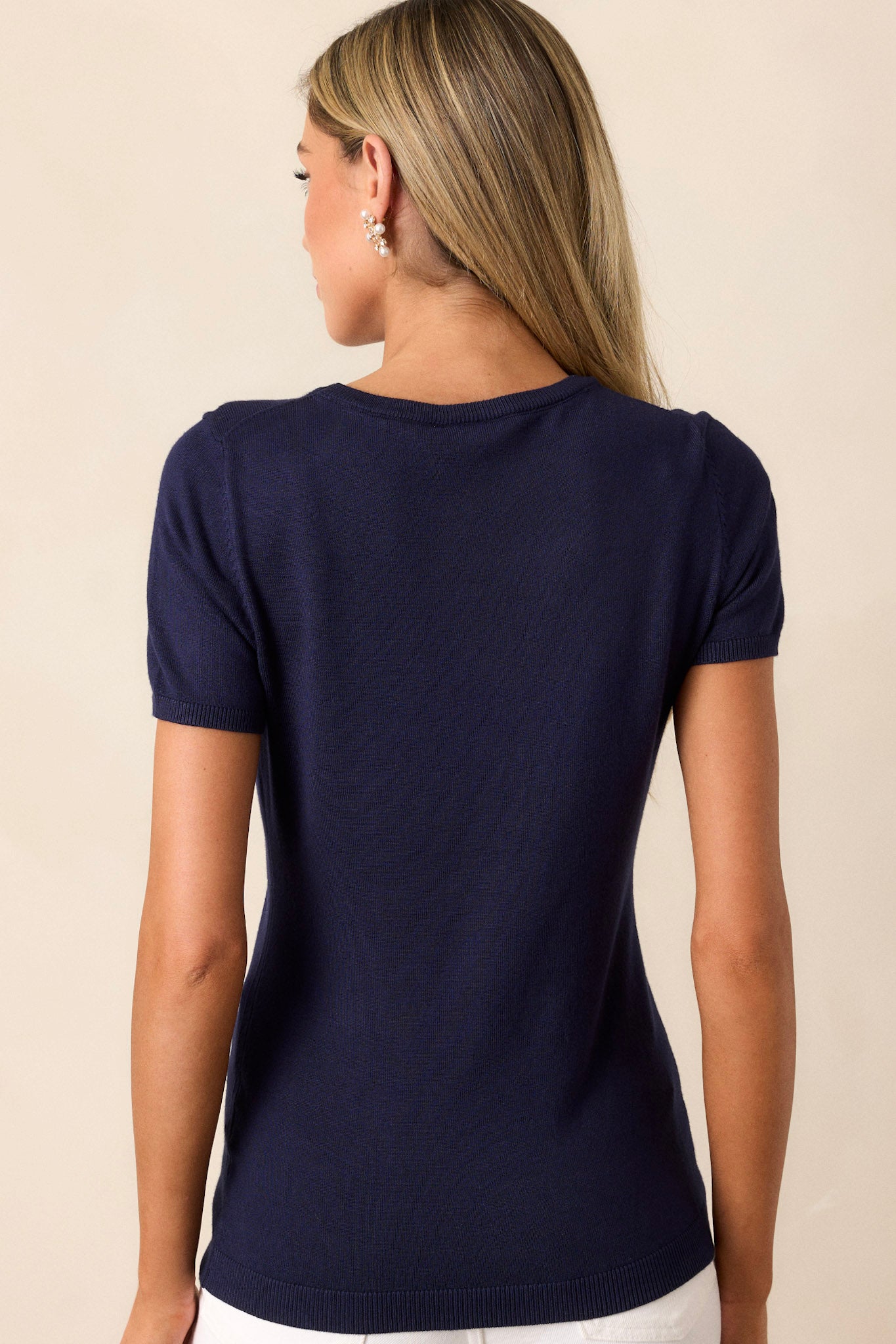 Back view of a navy sweater top highlighting the rounded neckline, soft sweater fabric, and ribbed hem.