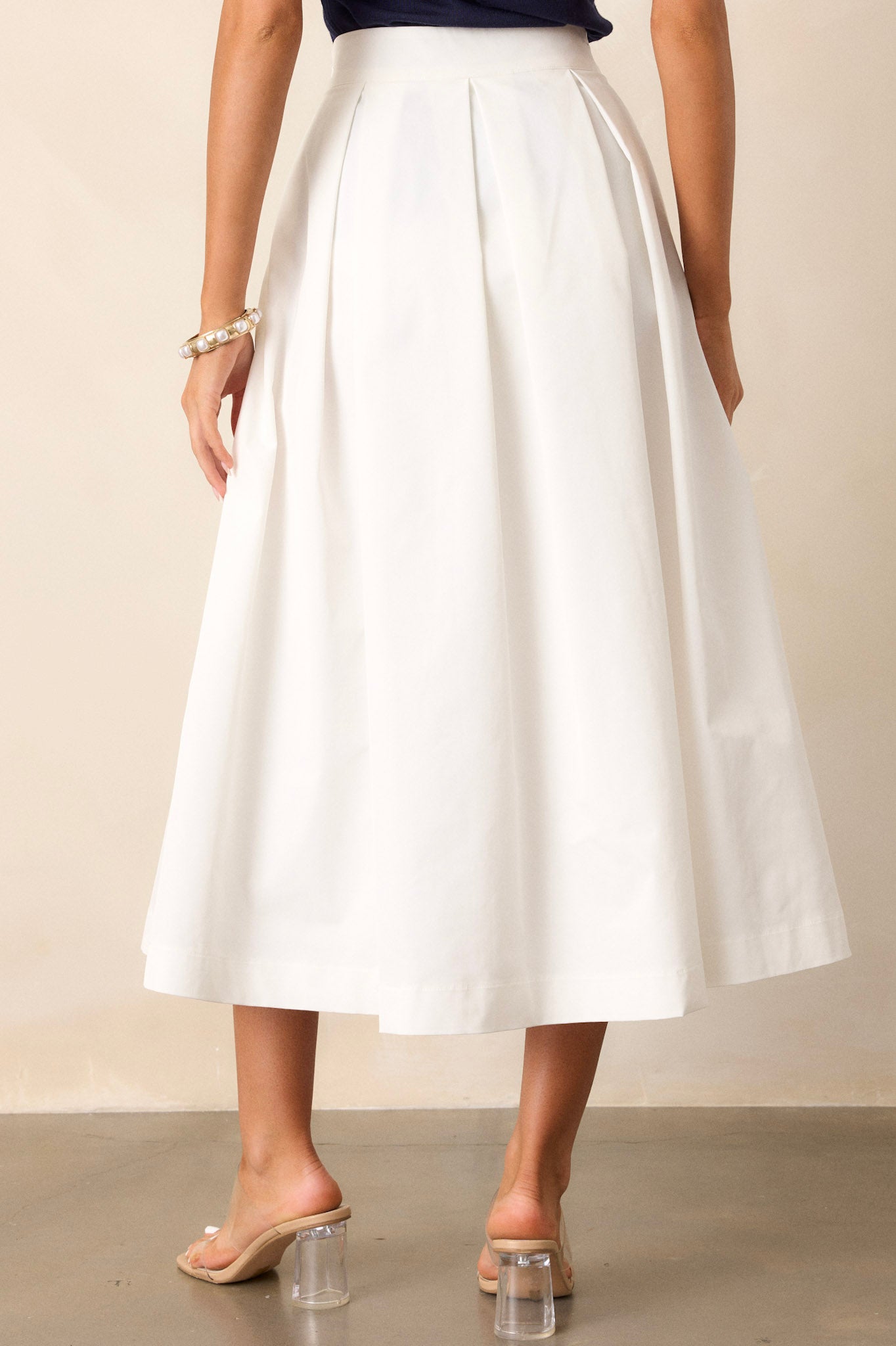 Back view of this white midi skirt that features a high waisted design, a discrete side zipper, and a thick waistline.