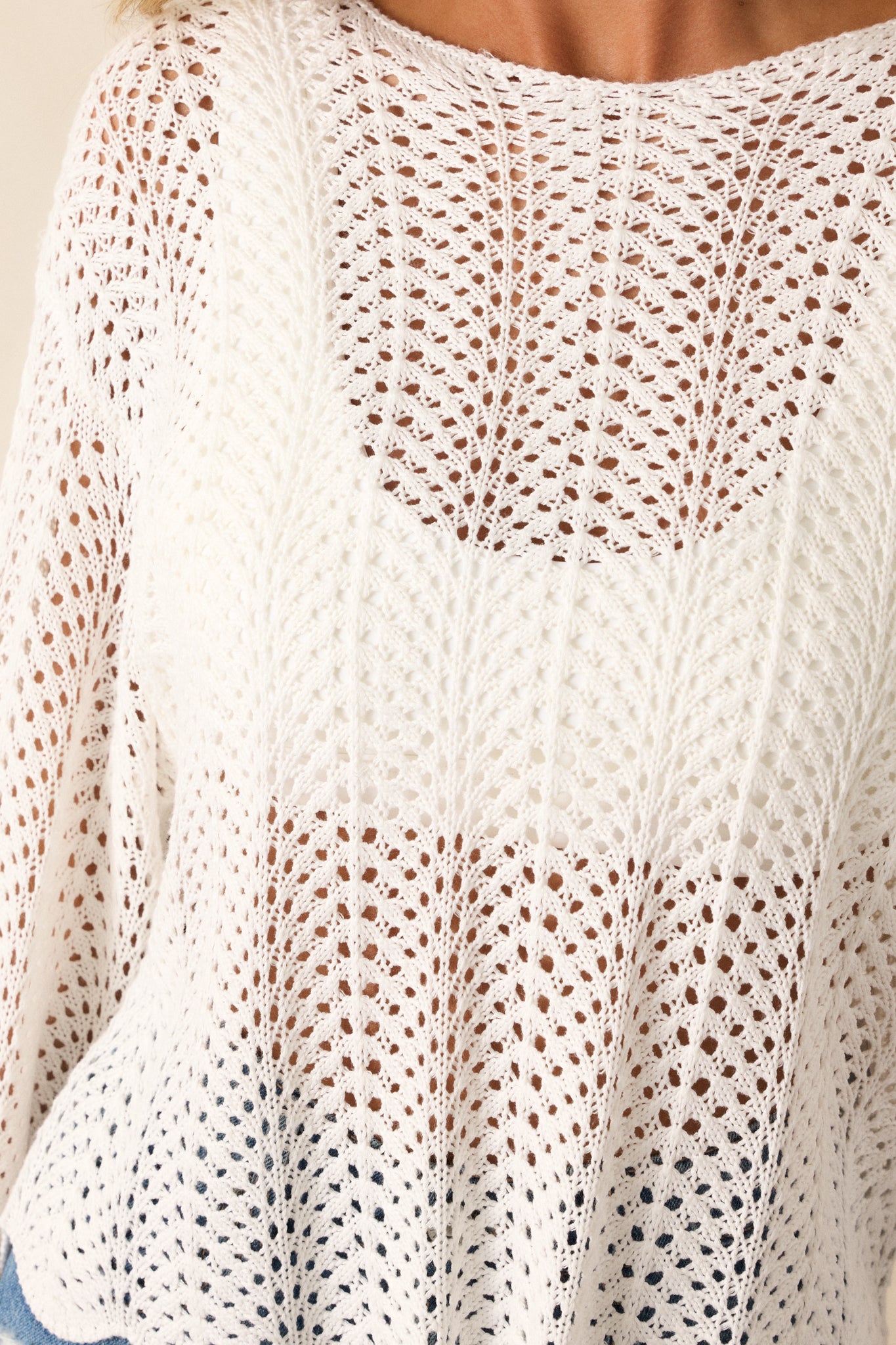 Close up view of this top that features a high rounded neckline, a soft material, an open-knit crochet design, scalloped long sleeves, and a scalloped hemline.