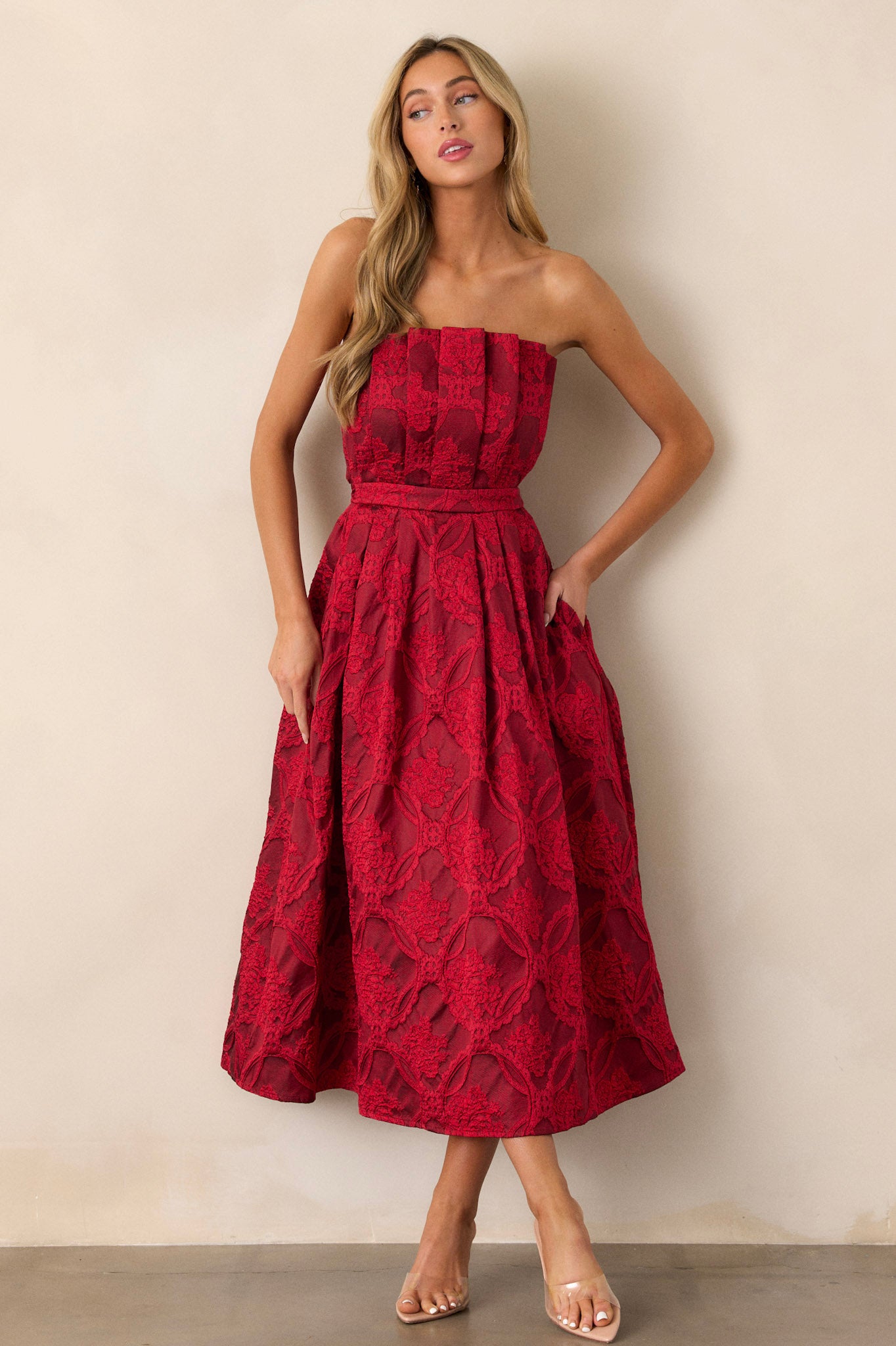 This red midi dress features a pleated bodice, a slightly pleated skirt, a jacquard design, functional hip pockets, a smocked back, a discrete back zipper and a strapless design.