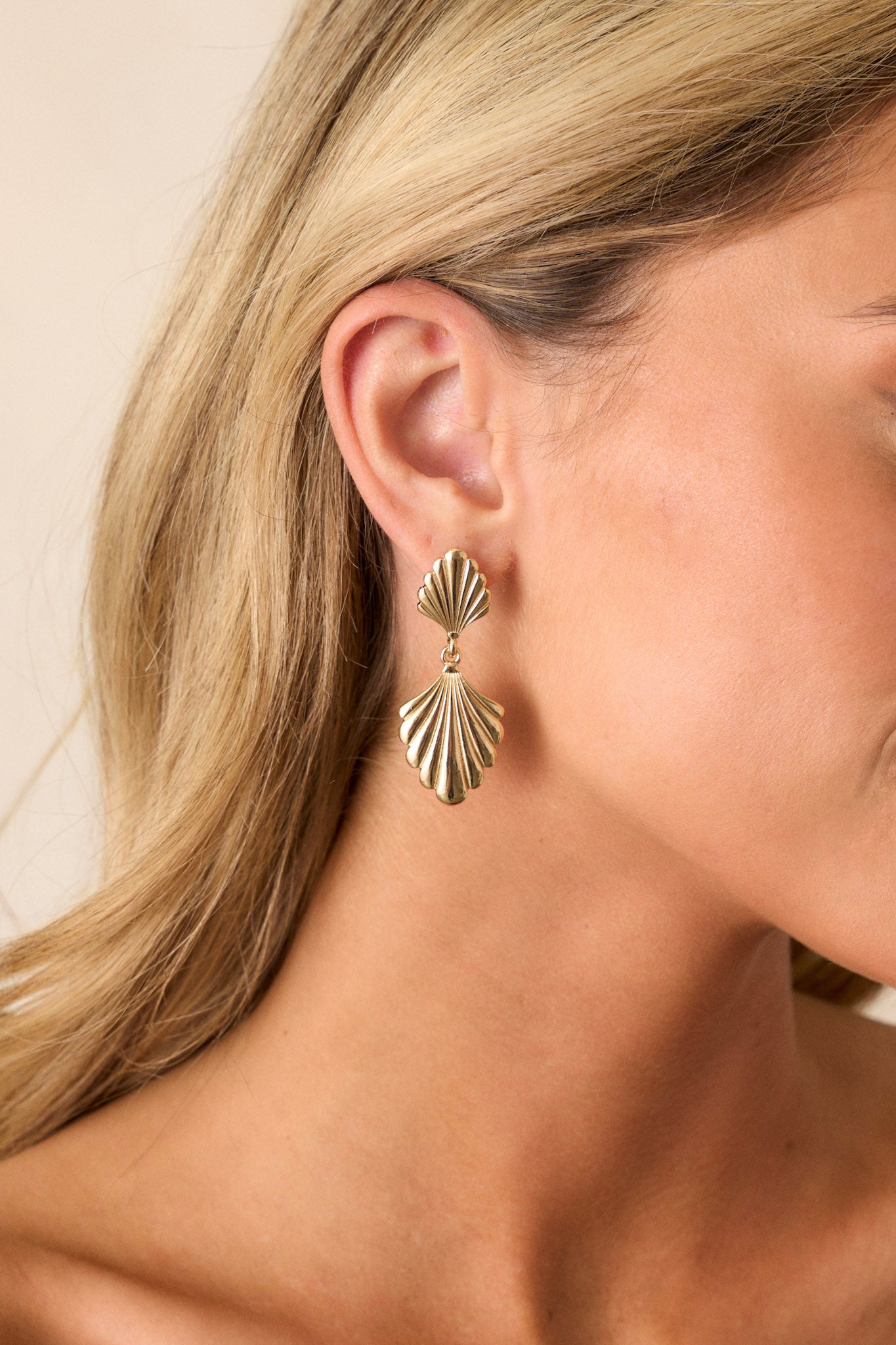 These gold earrings feature a tiered drop design, textured shell-like shapes, and secure post backings.