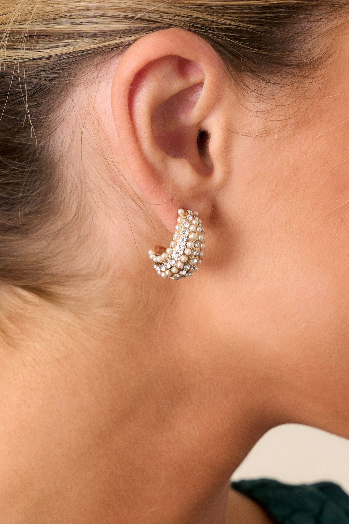 Side view of the gold earrings, highlighting the intricate arrangement of faux ivory pearls and rhinestones on the incomplete hoop design.