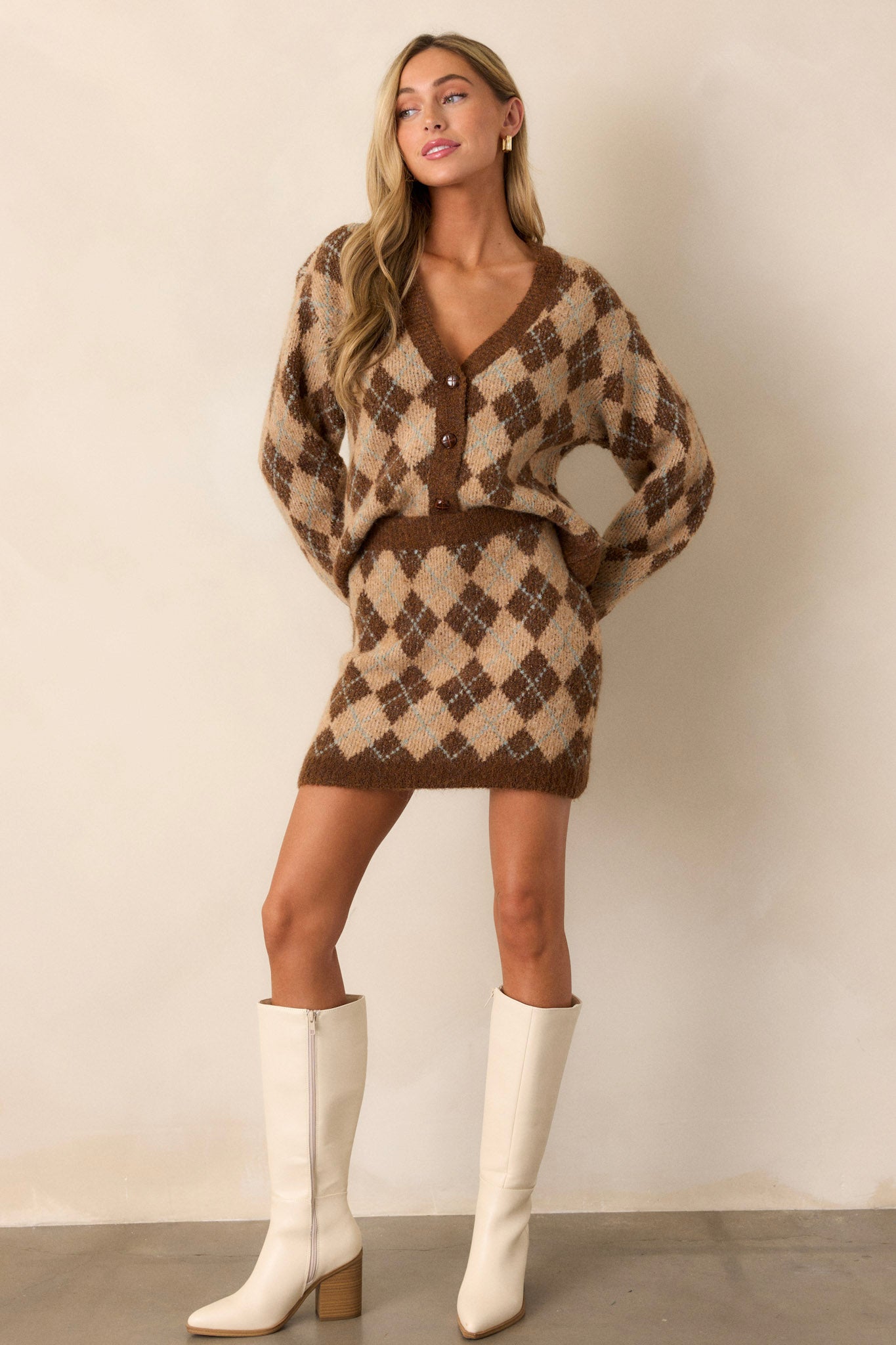 Full body view of a cozy knit cardigan featuring a warm brown argyle pattern, functional textured brown buttons up the front, a v-neckline, and a relaxed fit.