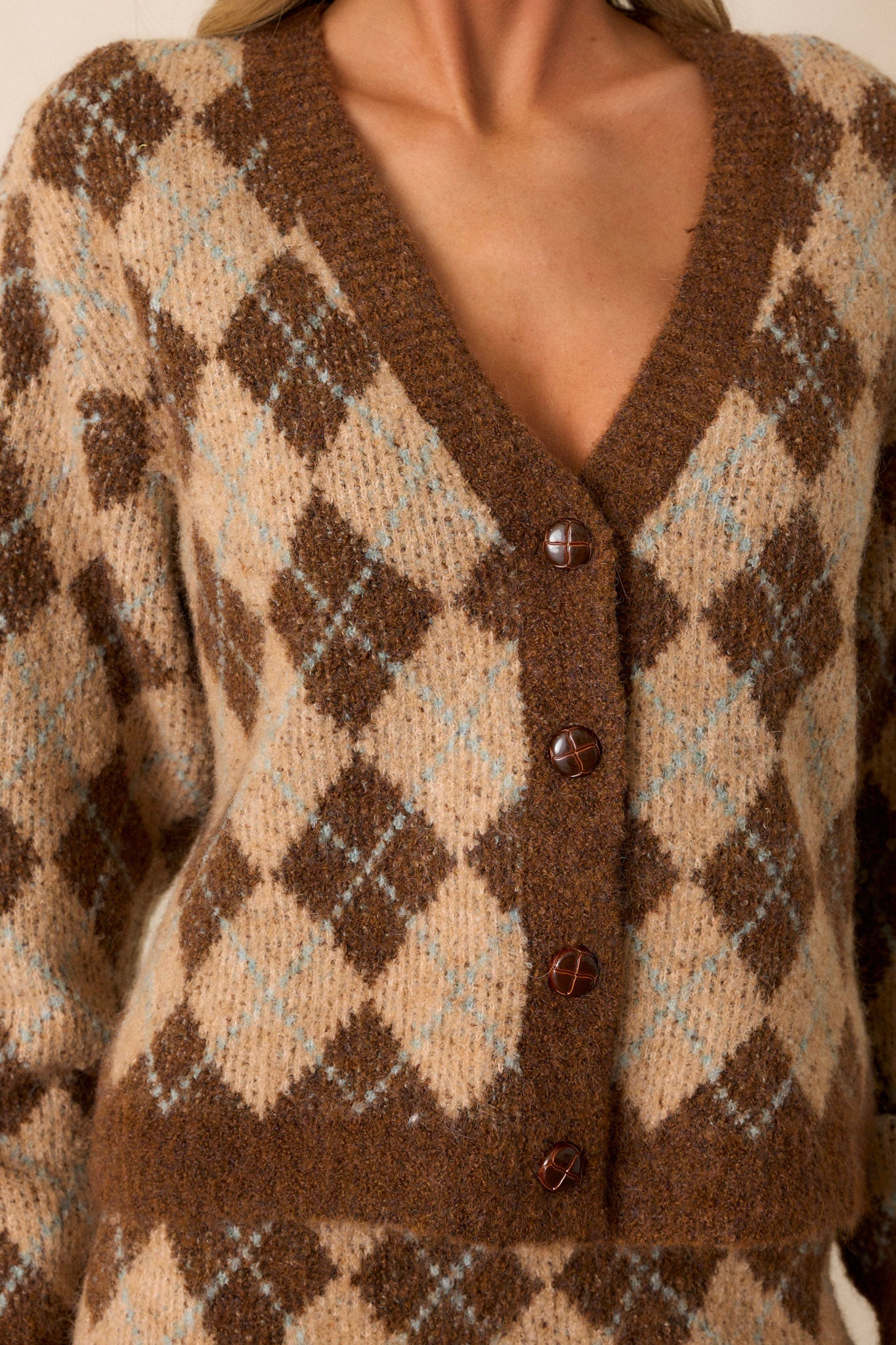 Close up of the textured brown functional buttons and v-neckline on this warm brown argyle cardigan. 