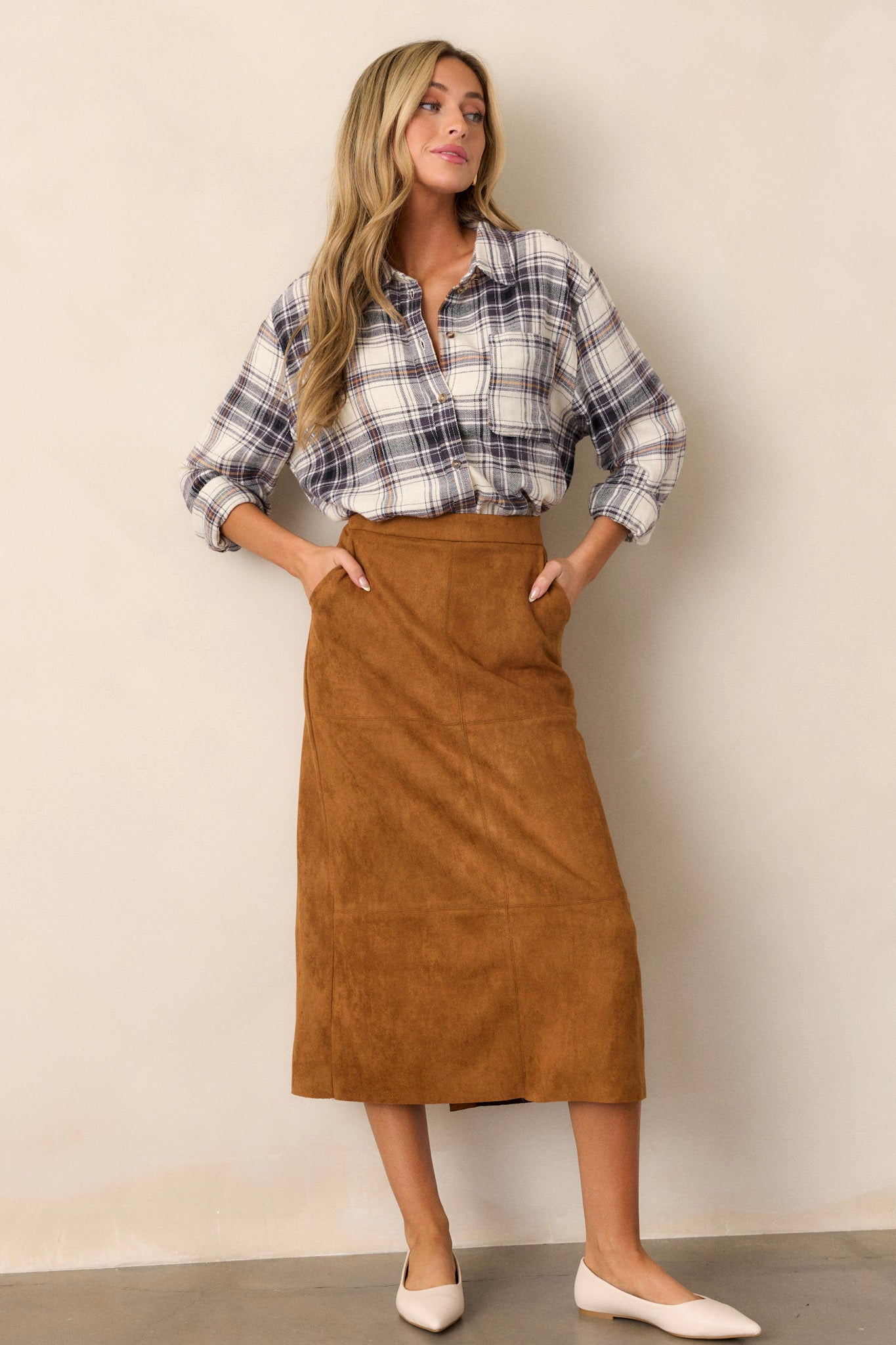 An A-line midi skirt, with a caramel color, faux suede material, functional pockets, and a small slit up the back of the skirt. 