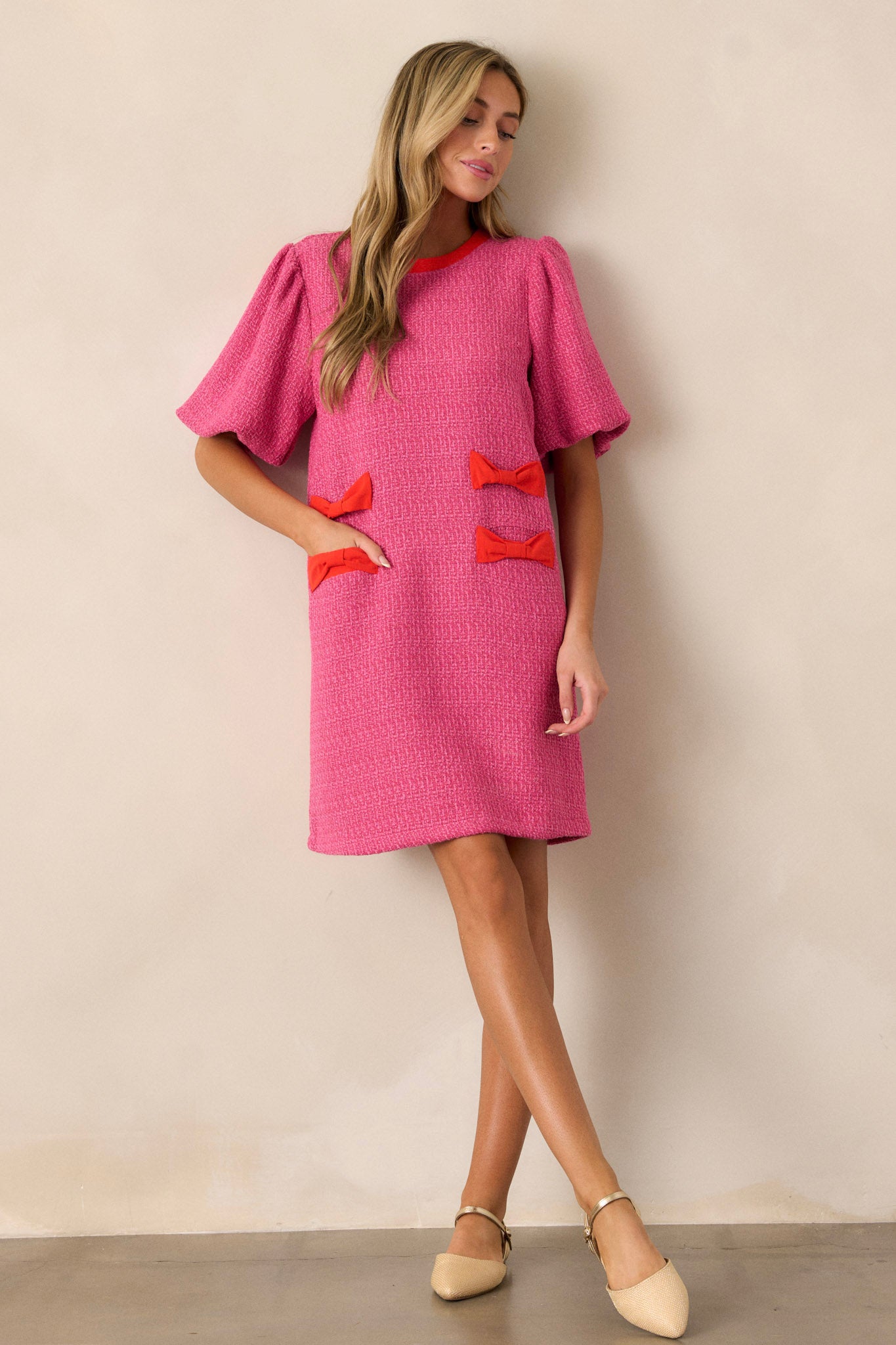 Action shot of the pink tweed dress showing how the fabric drapes and moves, highlighting the red bow detailing, functional hip pockets, and the relaxed fit.