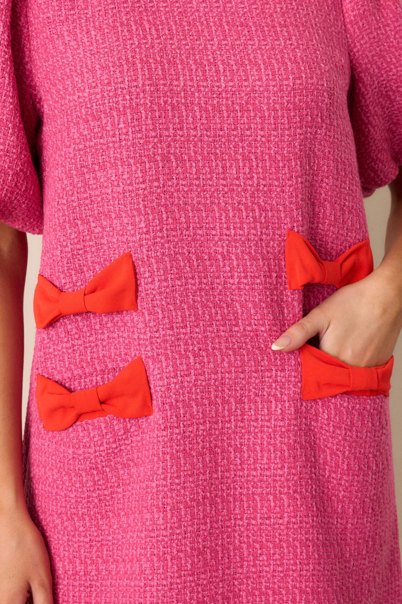 Close-up of the pink tweed dress focusing on the red bow detailing on the hips, the functional hip pockets, and the texture of the tweed fabric.