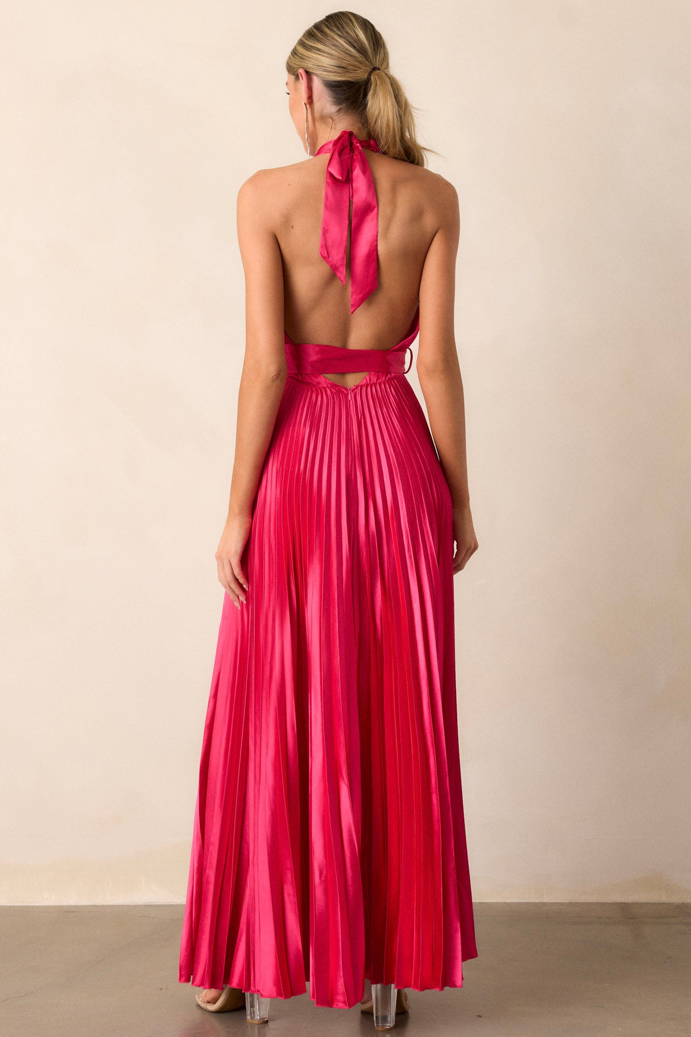 Back view of the magenta pink dress highlighting the halter neck tie, the functional zipper running down the back, and the flow of the pleats