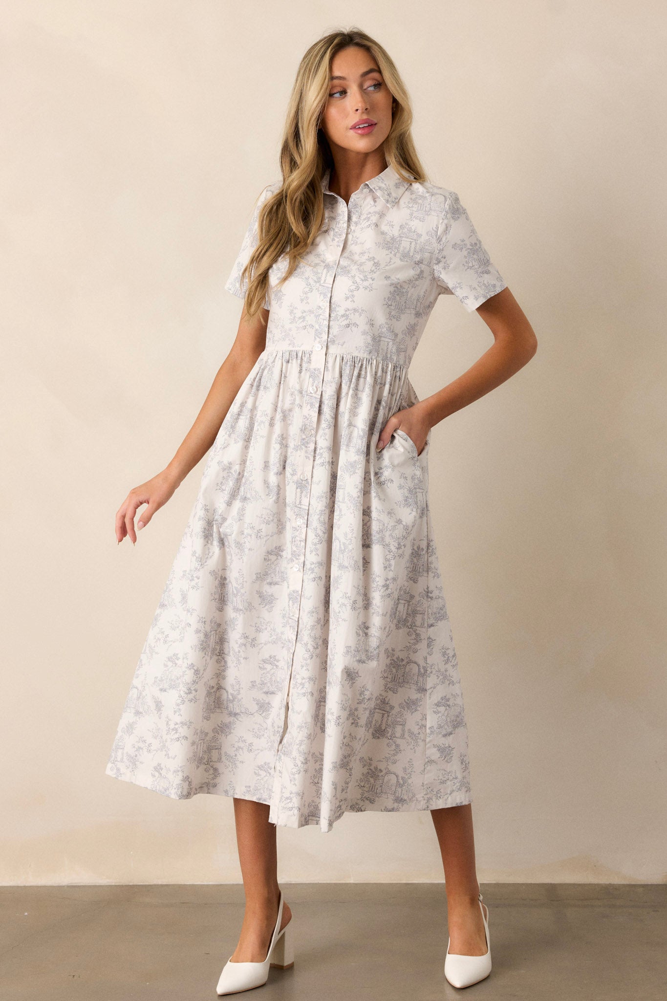 Action shot of a light grey maxi dress displaying the fit and movement, highlighting the collared neckline, functional button front, gathering at the waist, functional hip pockets, toile pattern, and flowing silhouette.