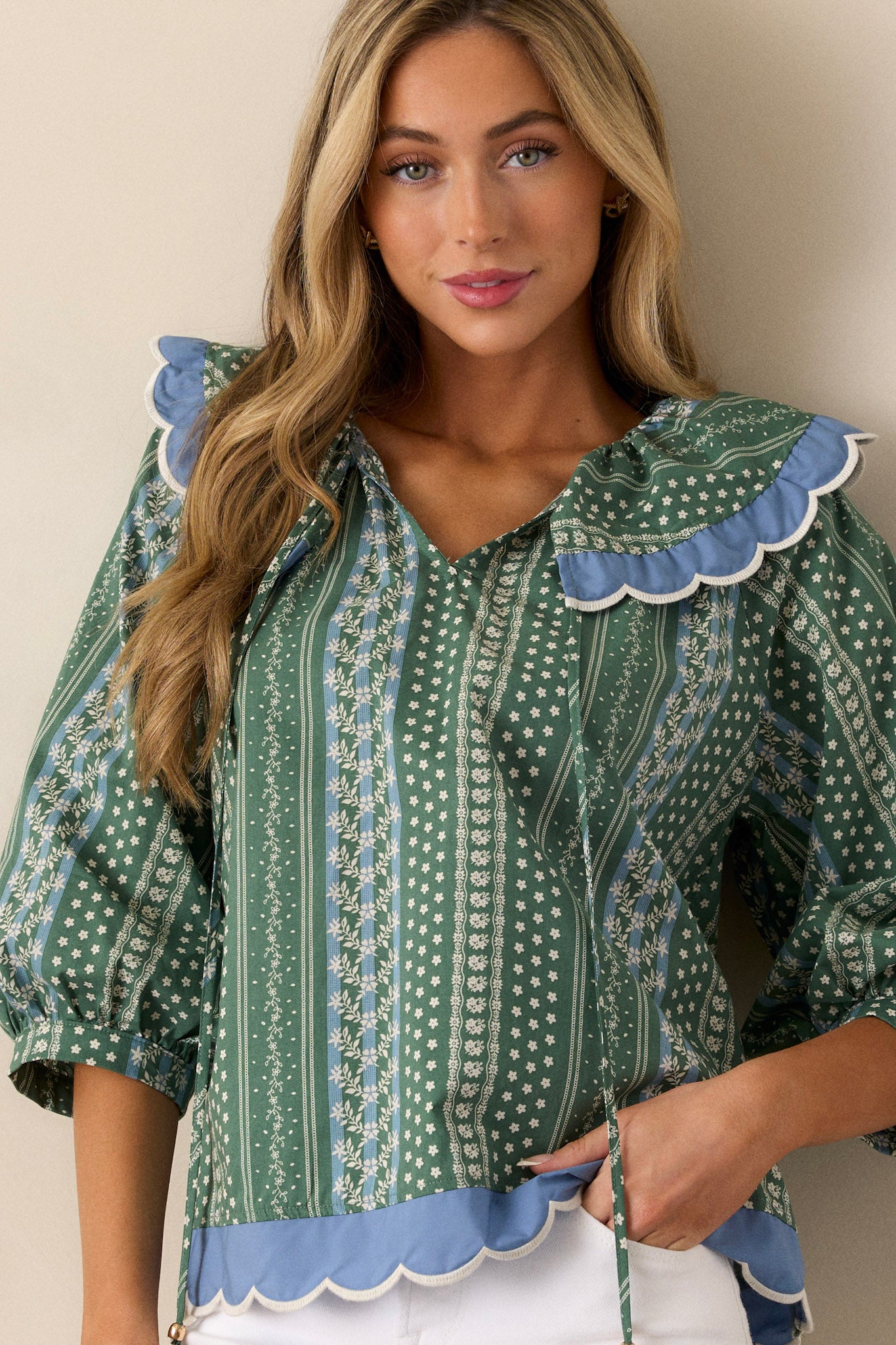 A green top with a scallop collar neckline, featuring 3/4 length cuffed sleeves and a delicate floral stripe print, along with a scallop bottom hem.