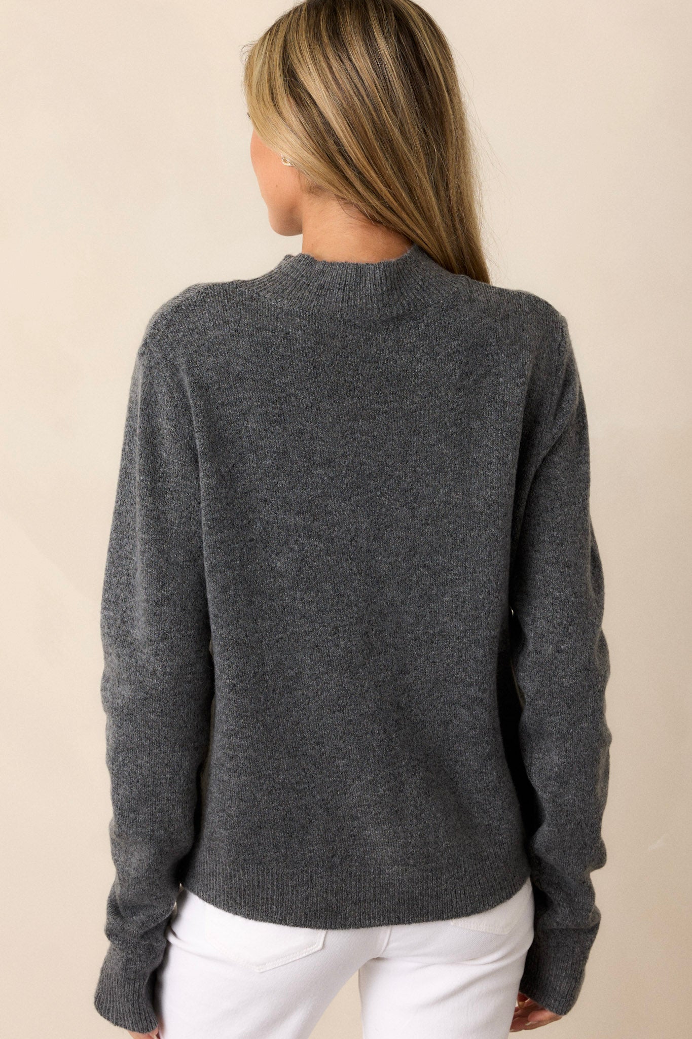 A rear view of the sweater, displaying the clean lines of the back and the continuation of the ribbed detailing along the hemline and cuffs.