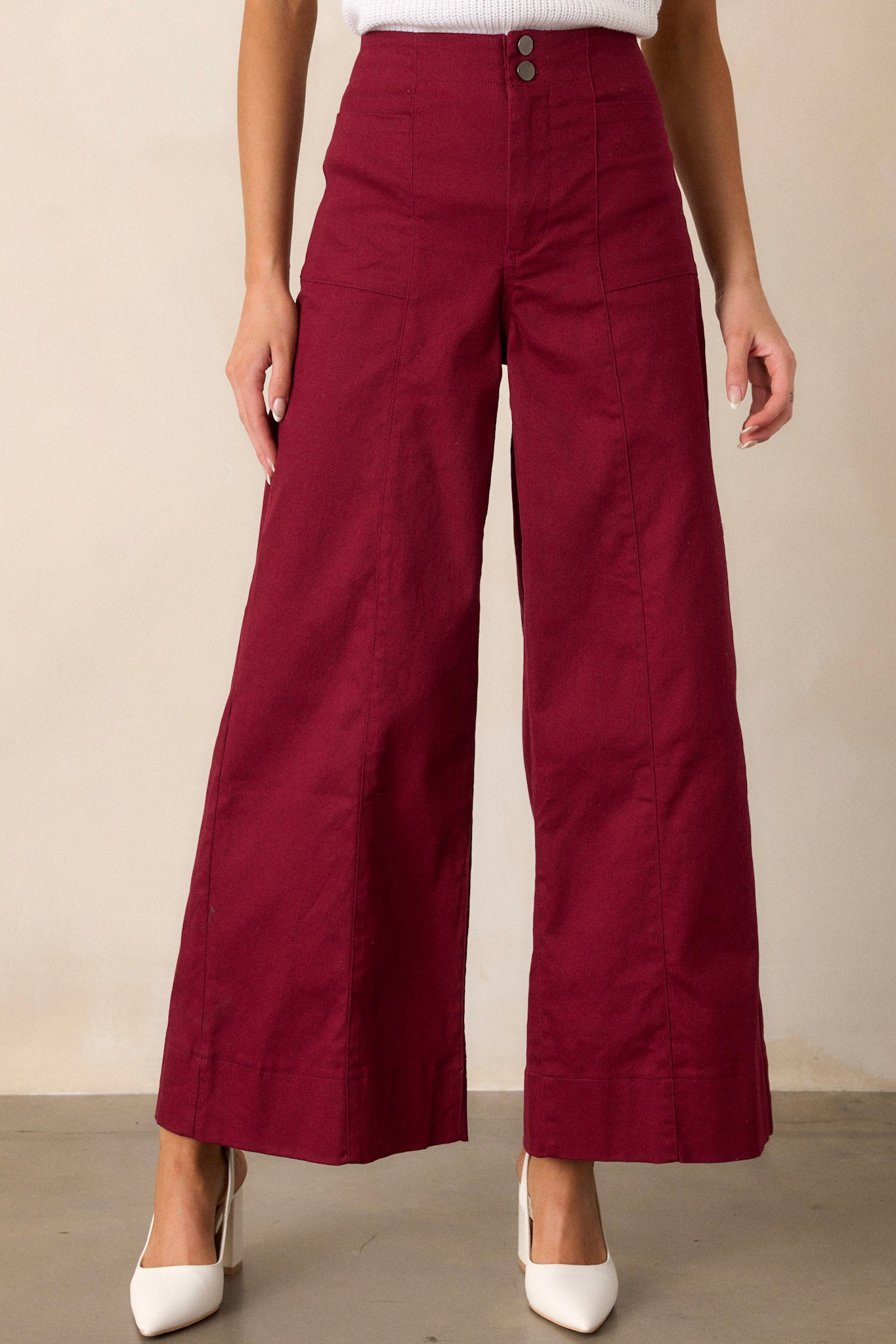 Front view of burgundy pants featuring a high waisted design, a button zipper closure, functional rectangular hip pockets, and a wide leg.