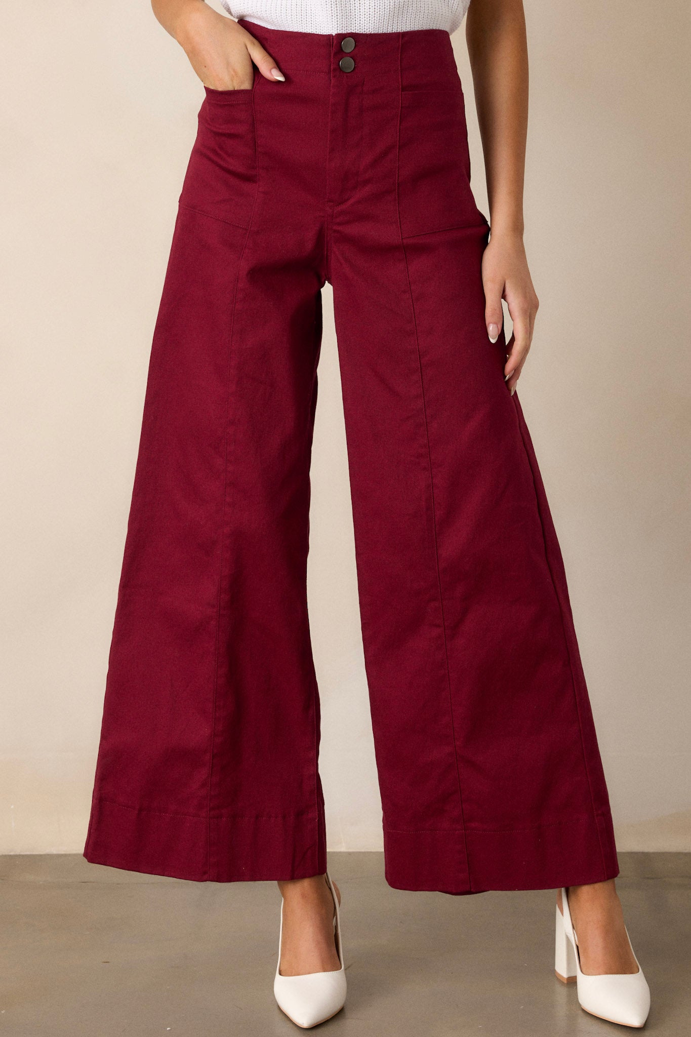 Close-up of burgundy pants showing the button zipper closure and functional rectangular hip pockets.