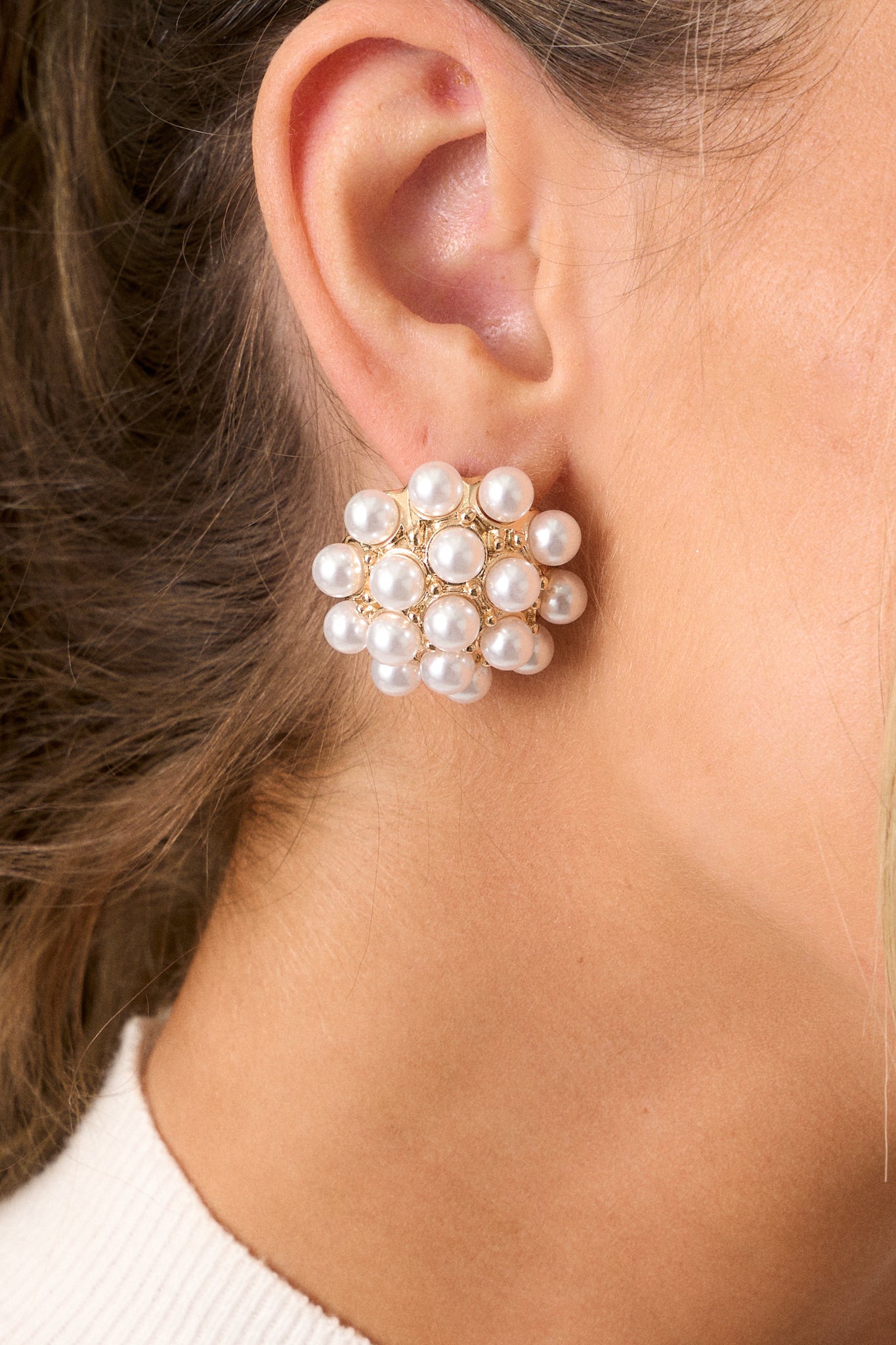 Close-up view of these earrings featuring gold hardware, faux ivory pearl clusters, a dome-like shape, and secure post backings.