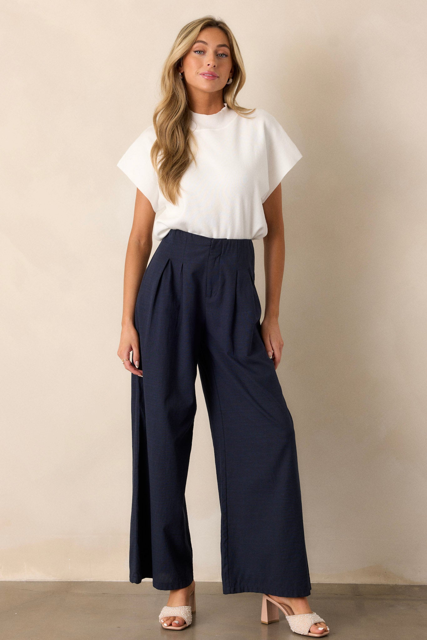 Full body view of navy straight leg pants displaying the fit and movement, highlighting the high waisted design, button zipper closure, slight pleats, and functional hip pockets.