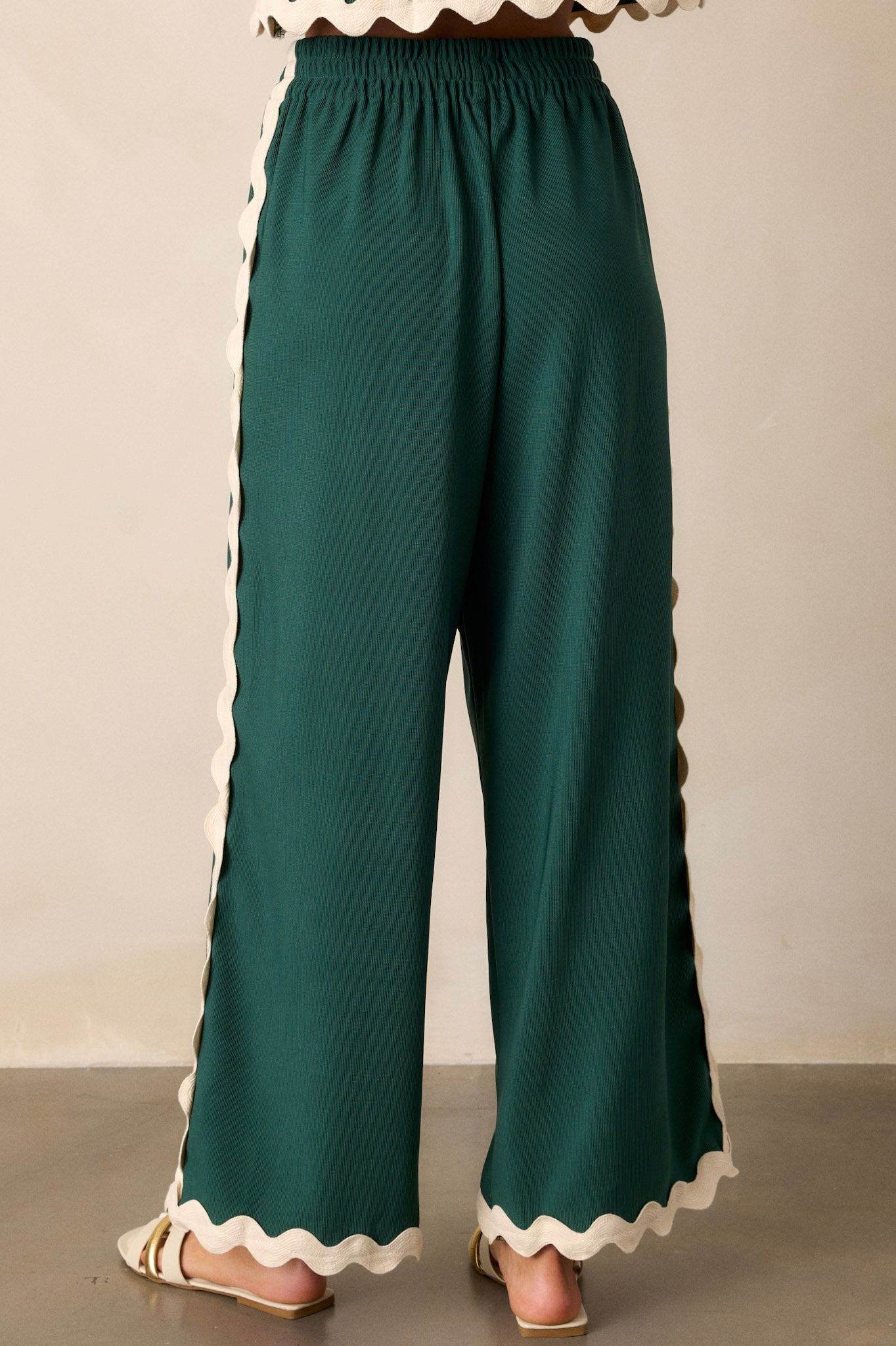 Back view of green pants highlighting the overall fit, elastic waistband, ribbed texture, and ricrac hemlines.