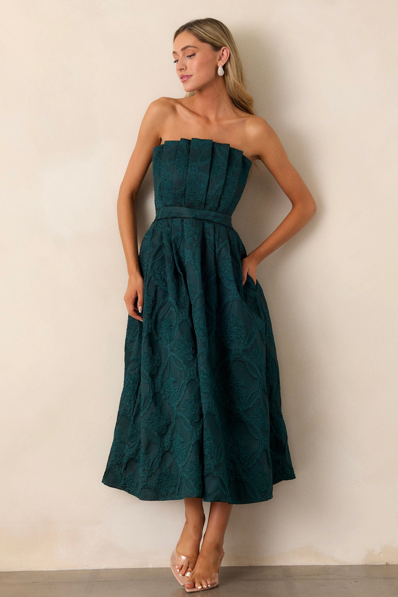 Front view of the green dress highlighting the structured pleated bodice and strapless neckline, with the smooth transition into the slightly pleated skirt.