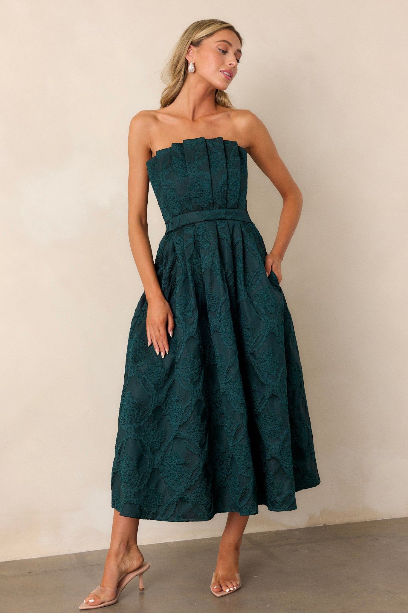 Green dress featuring a strapless design with a pleated bodice, slightly pleated skirt, and functional hip pockets.