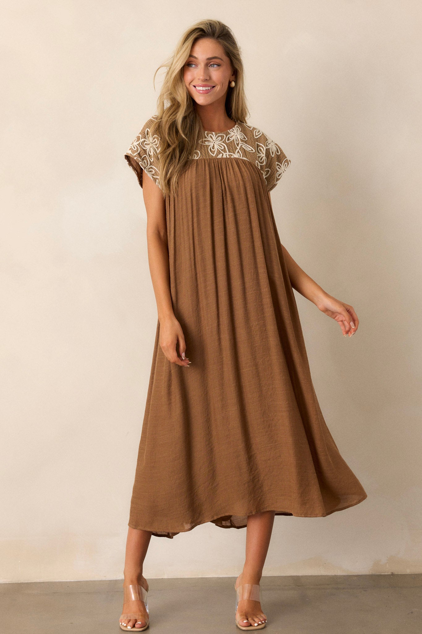 Front angled view of the tan midi dress showcasing a high rounded neckline, embroidered floral pattern, and short sleeves.