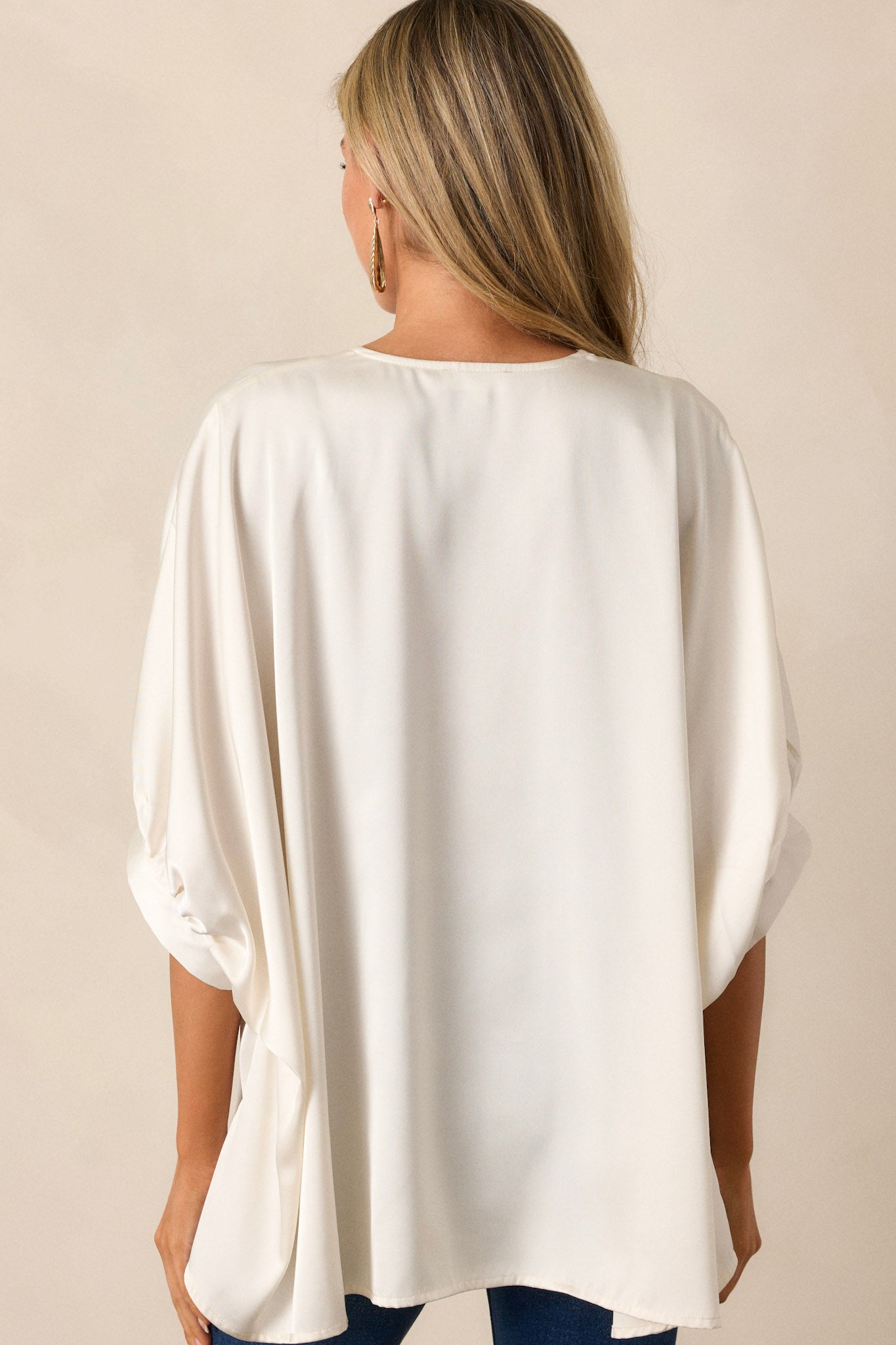 Back view of a white top highlighting the overall fit, wide, flowy design, and satin-like material.