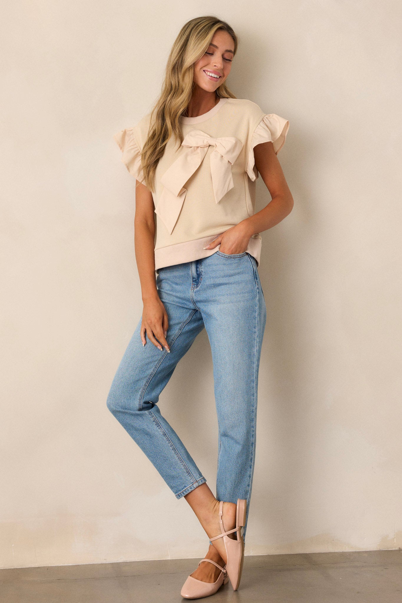 A beige top with a crew neckline, featuring ruffle short sleeves and a bow accent on the front.