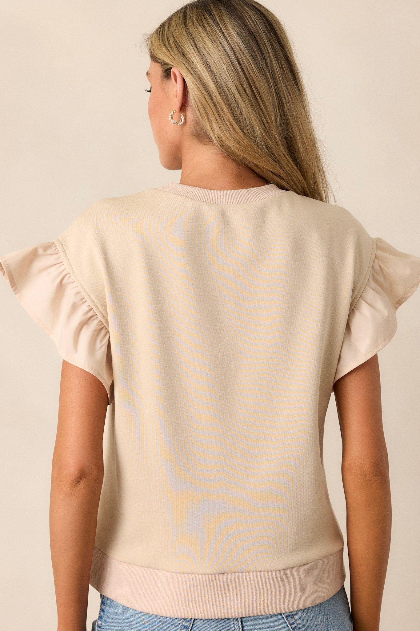 The back of the beige top, featuring a simple, clean design with a smooth fit and visible ruffle sleeve details.