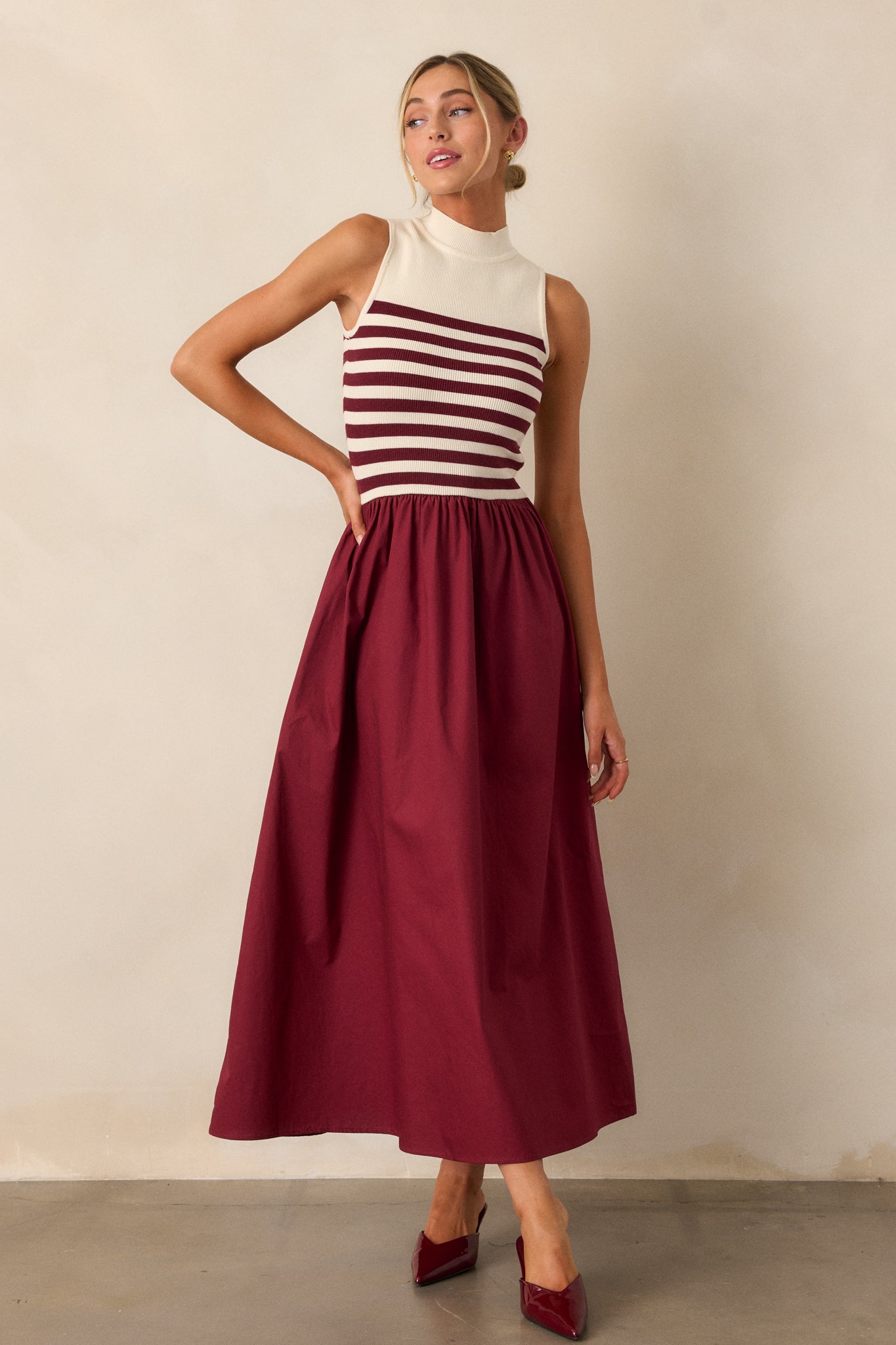 Angled full body view of this burgundy stripe maxi dress that features a high neckline, a striped sweater bodice, and a flowy skirt.