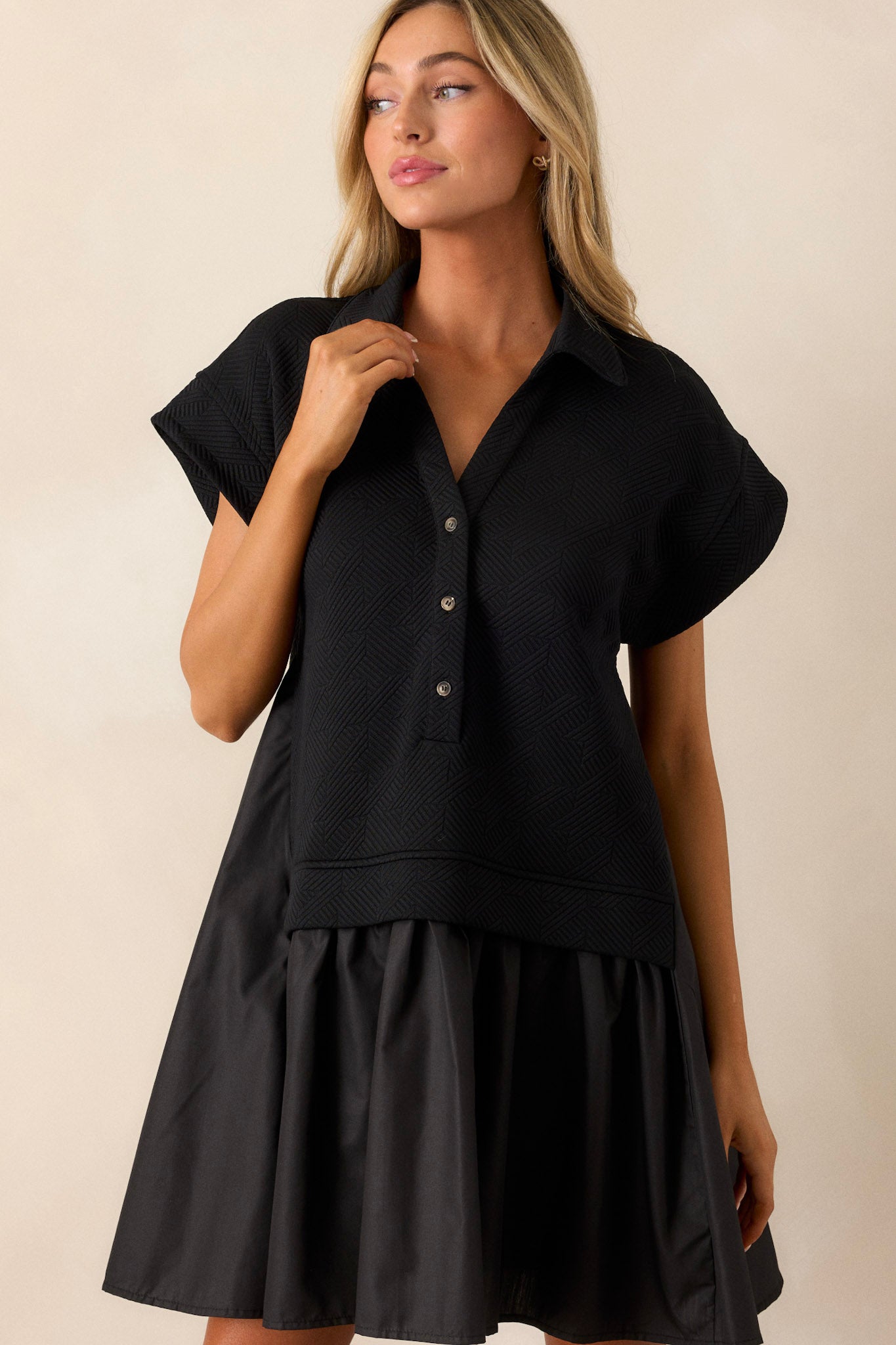 This black quilted dress features a collared v-neckline, a functional button front, a quilted bodice, a tiered design and short sleeves.