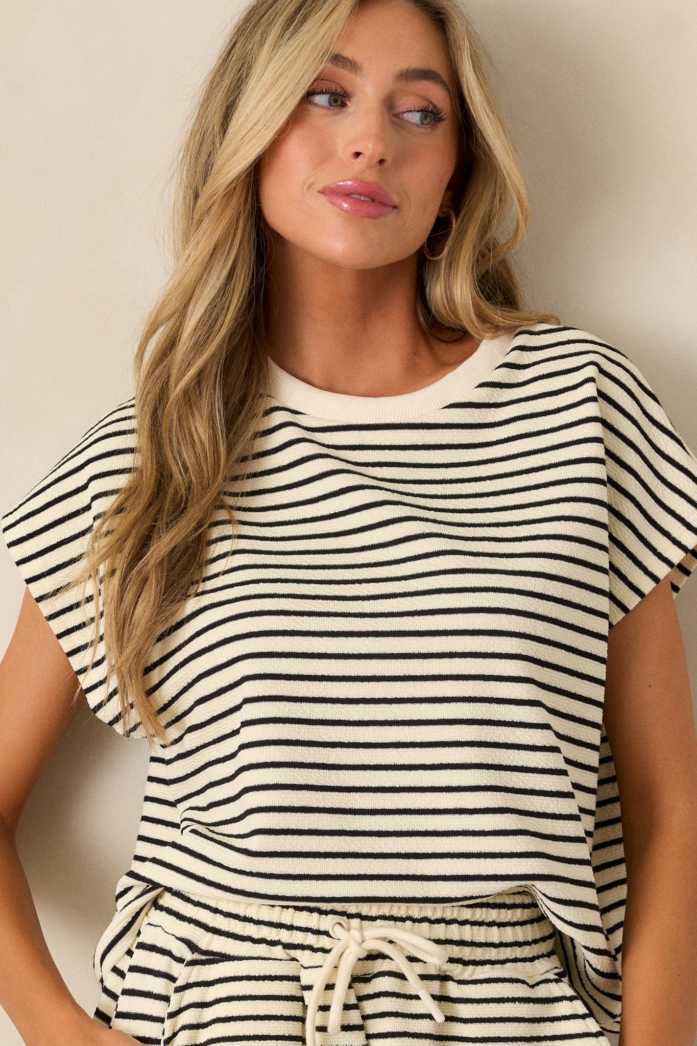 Front angled view of an ivory top featuring cap sleeves, a ribbed neckline, and a boxy fit