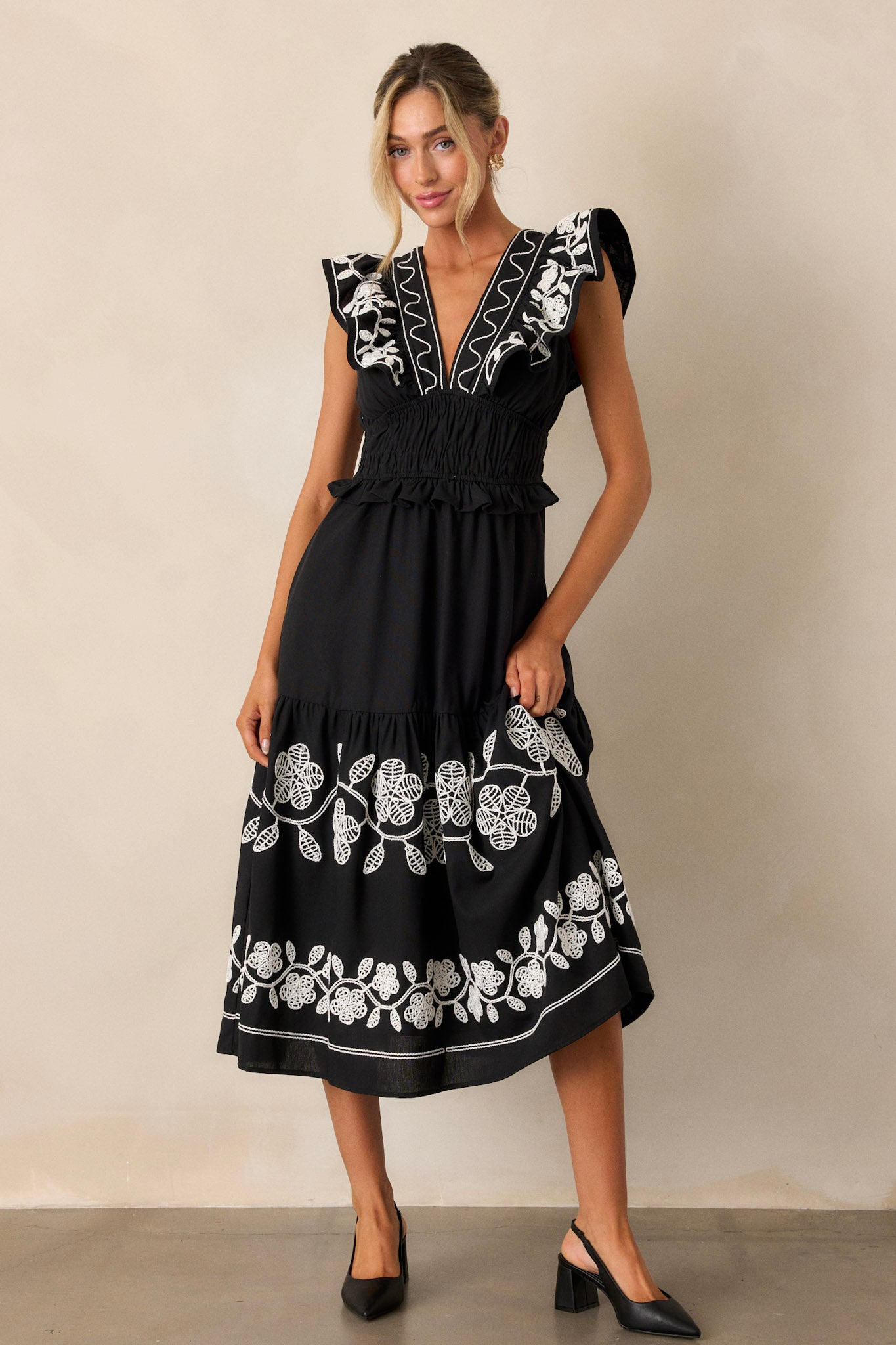 Full-body image highlighting the embroidered detailing throughout the black dress, with focus on the functional hip pockets.