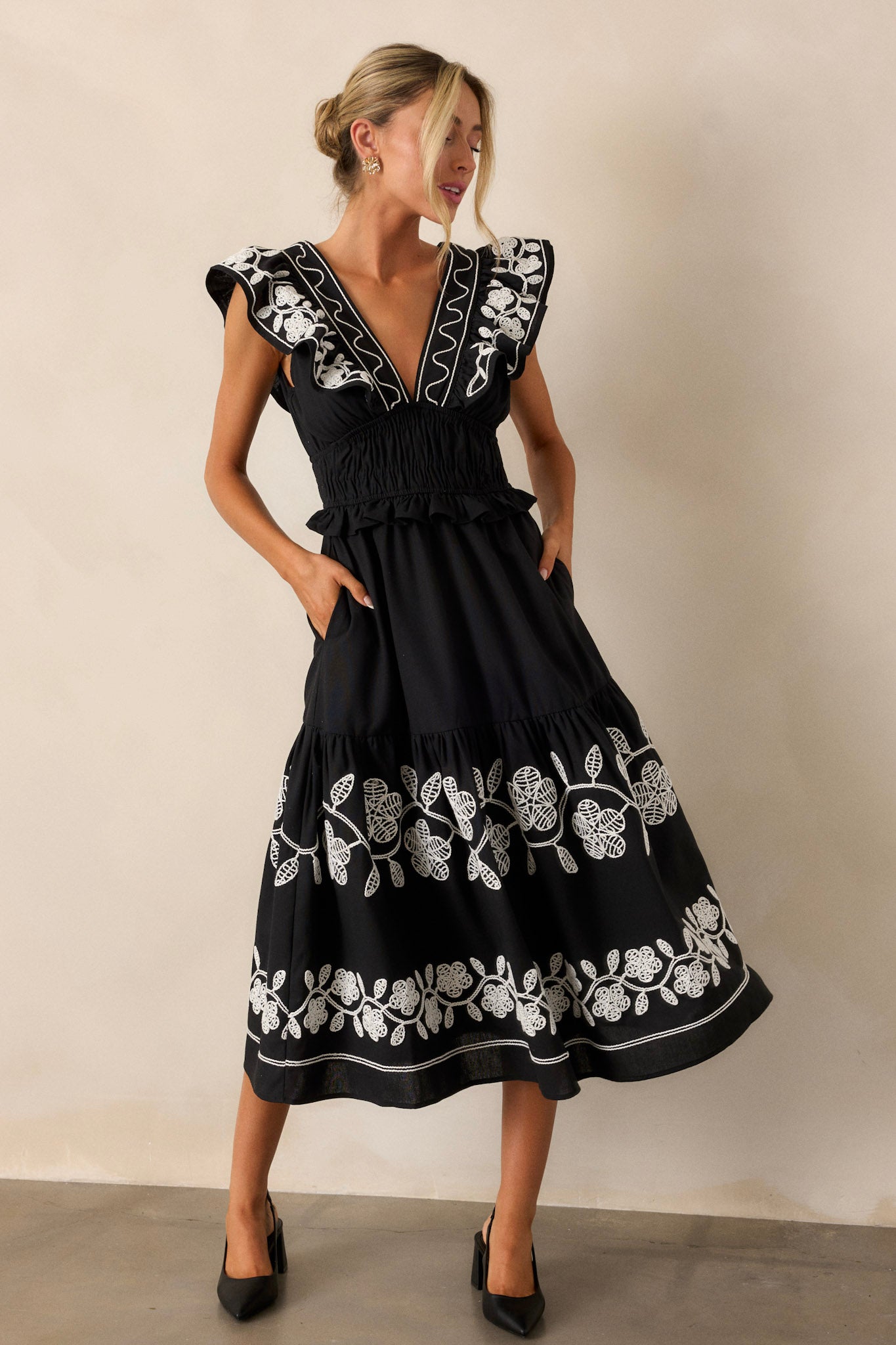 Full-body image emphasizing the plunging neckline and the detailed embroidery on the bodice of the black dress.