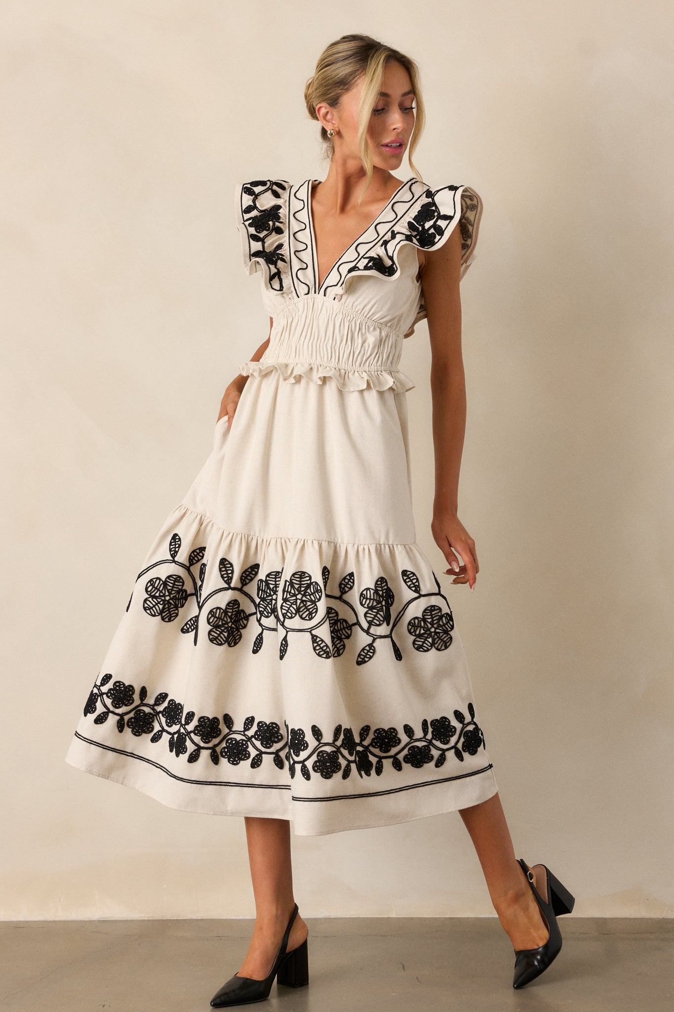 Full-body image emphasizing the plunging neckline and the detailed embroidery on the bodice of the beige dress.