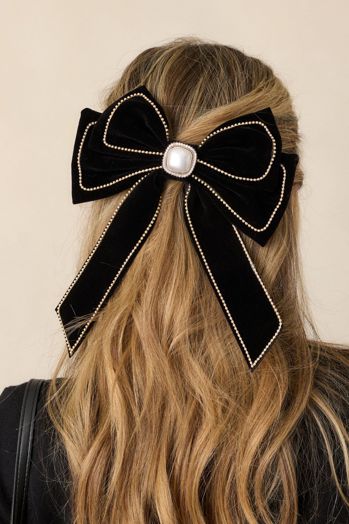 A close-up of a black velvet bow clip with a tiny pearl and gold chain trim, featuring a large faux ivory pearl at the center with a rhinestone border.