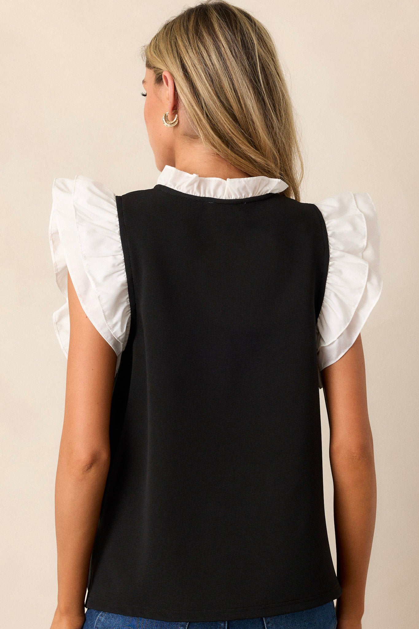 Back view of the top highlighting the continuation of the ribbed design and the side slits in the hem, with the ruffled collar adding a stylish detail