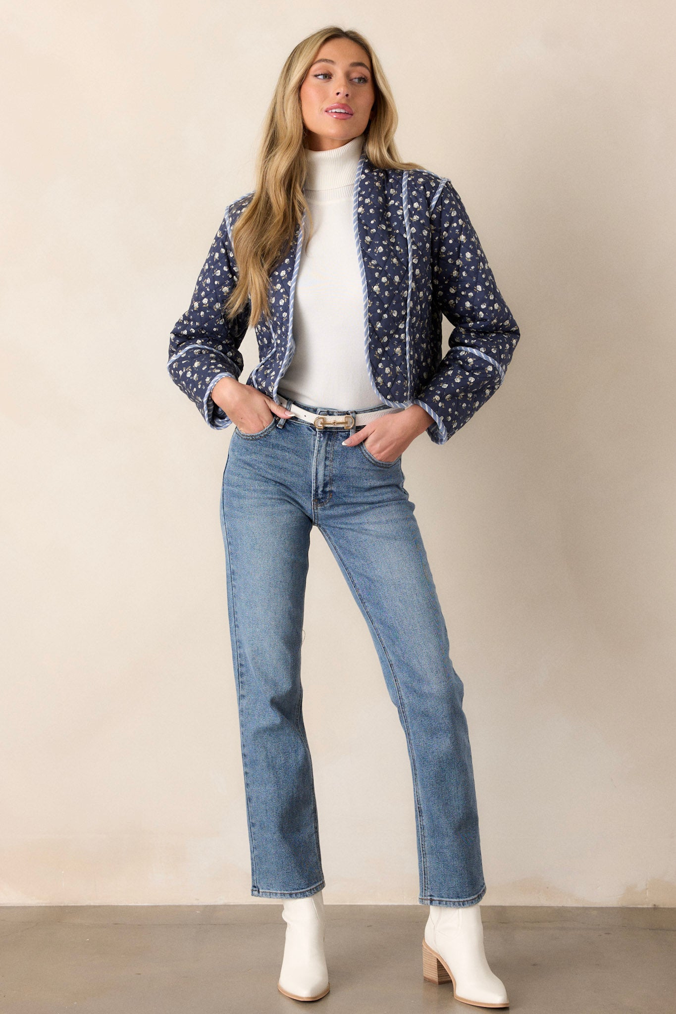 Angled full body view of this navy jacket that features an open front, a rounded neckline, a small floral pattern, a blue and white striped interior, a quilted material, a blue and white striped trim and long sleeves.