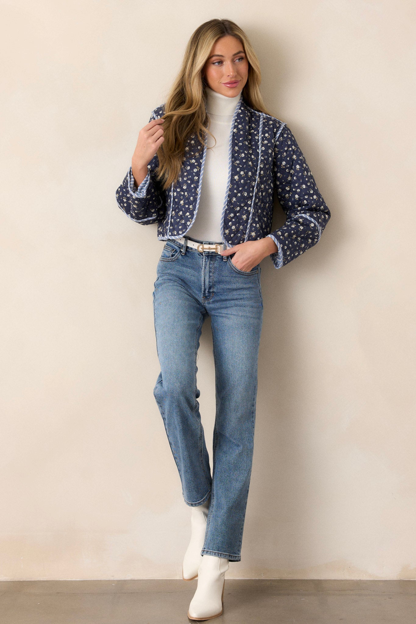 Front view of this navy jacket that features an open front, a rounded neckline, a small floral pattern, a blue and white striped interior, a quilted material, a blue and white striped trim and long sleeves.