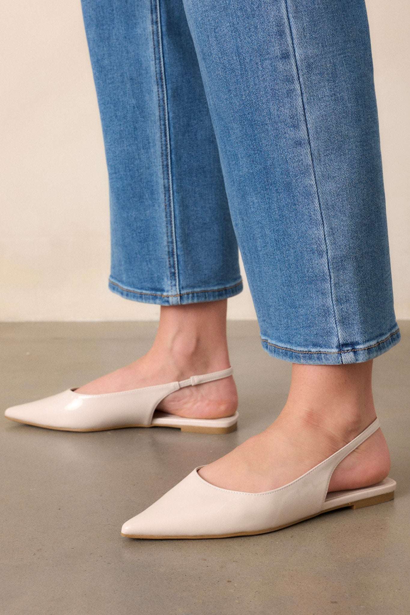 Close-up of these ivory flats that feature a pointed toe, a faux leather texture, a slingback-style strap, and a sleek ivory color.