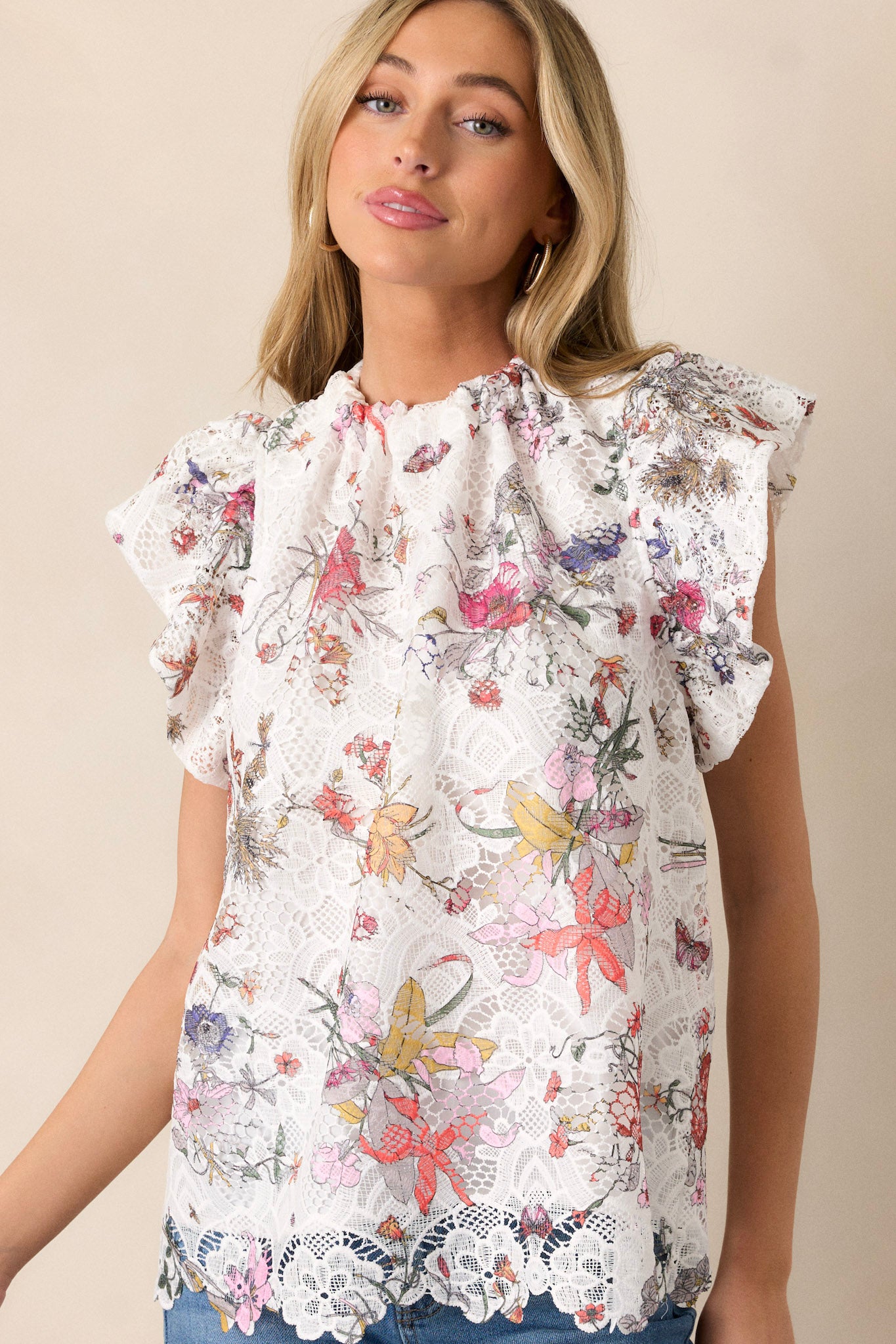 Front view of a white top featuring a high neckline, a self-tie feature at the back of the neck, a floral lace overlay, and ruffled short sleeves.