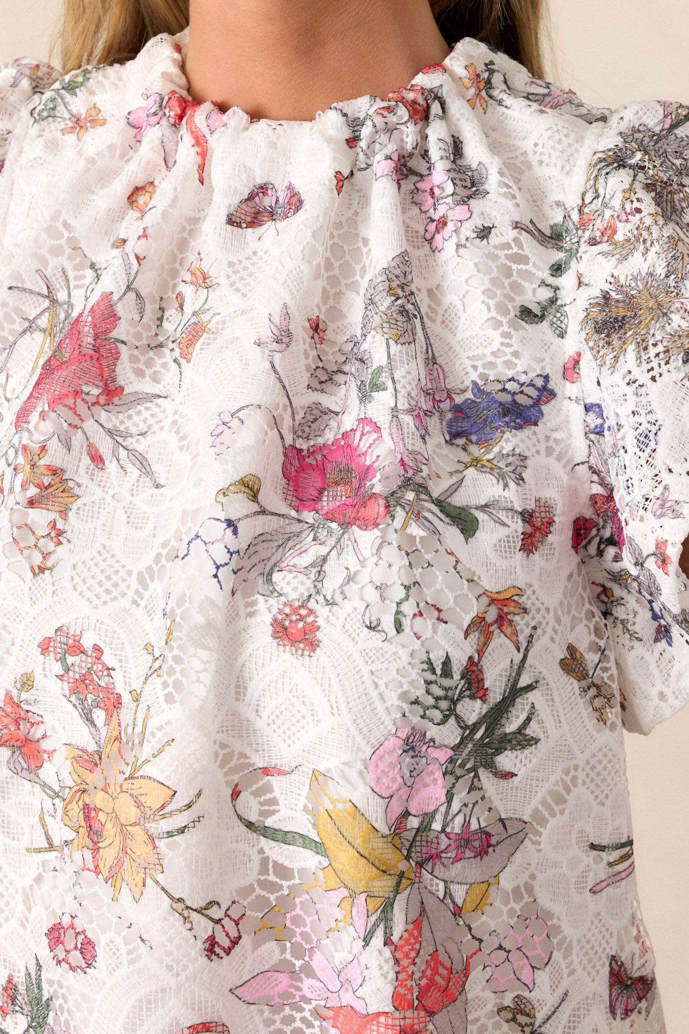 Close-up of the white top showing the high neckline, floral lace overlay, and ruffled short sleeves.