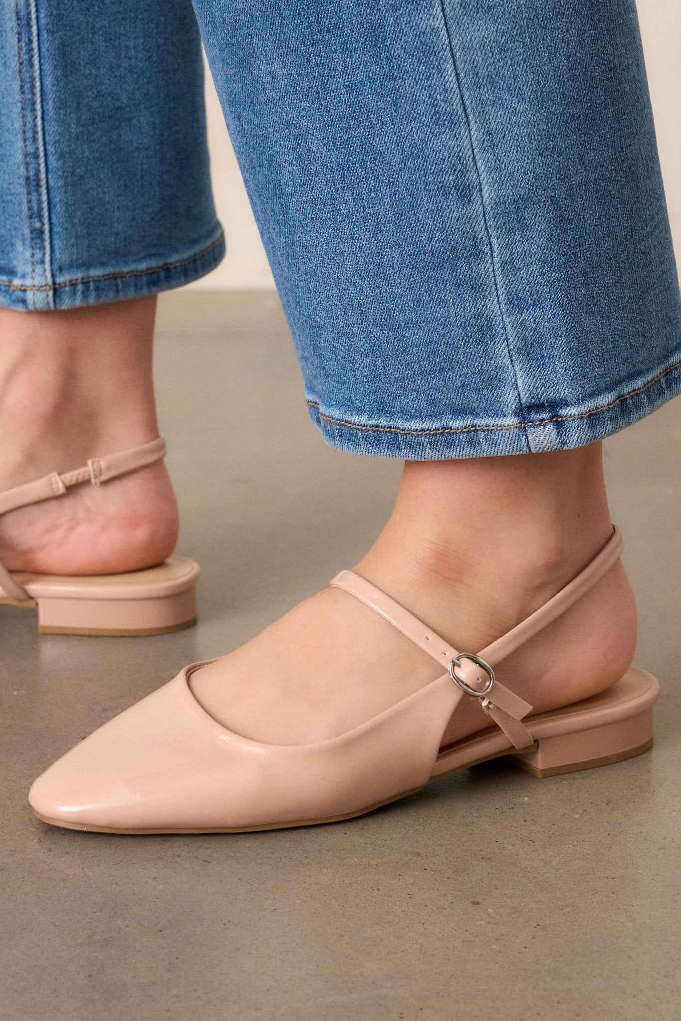 Close-up of these beige flats that feature a slightly squared toe, an across the foot strap with a silver buckle, an ankle strap, a small platform, and a shiny beige finish.