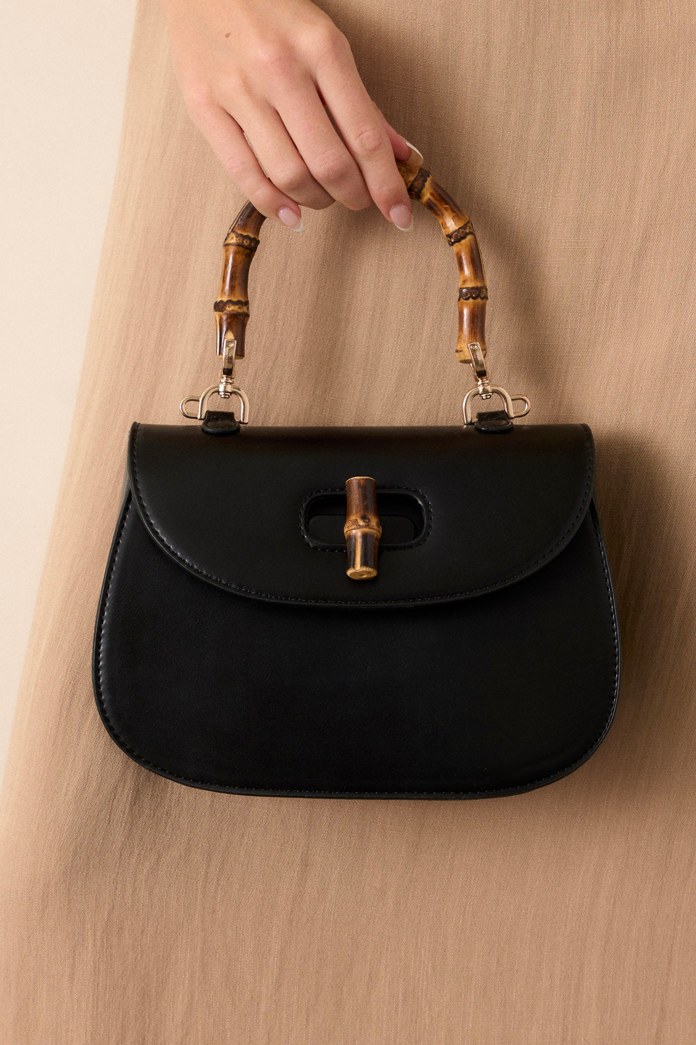 Close up view of this black handbag that features a single flap design, a bamboo top handle, a bamboo twist lock closure, and a removable strap.