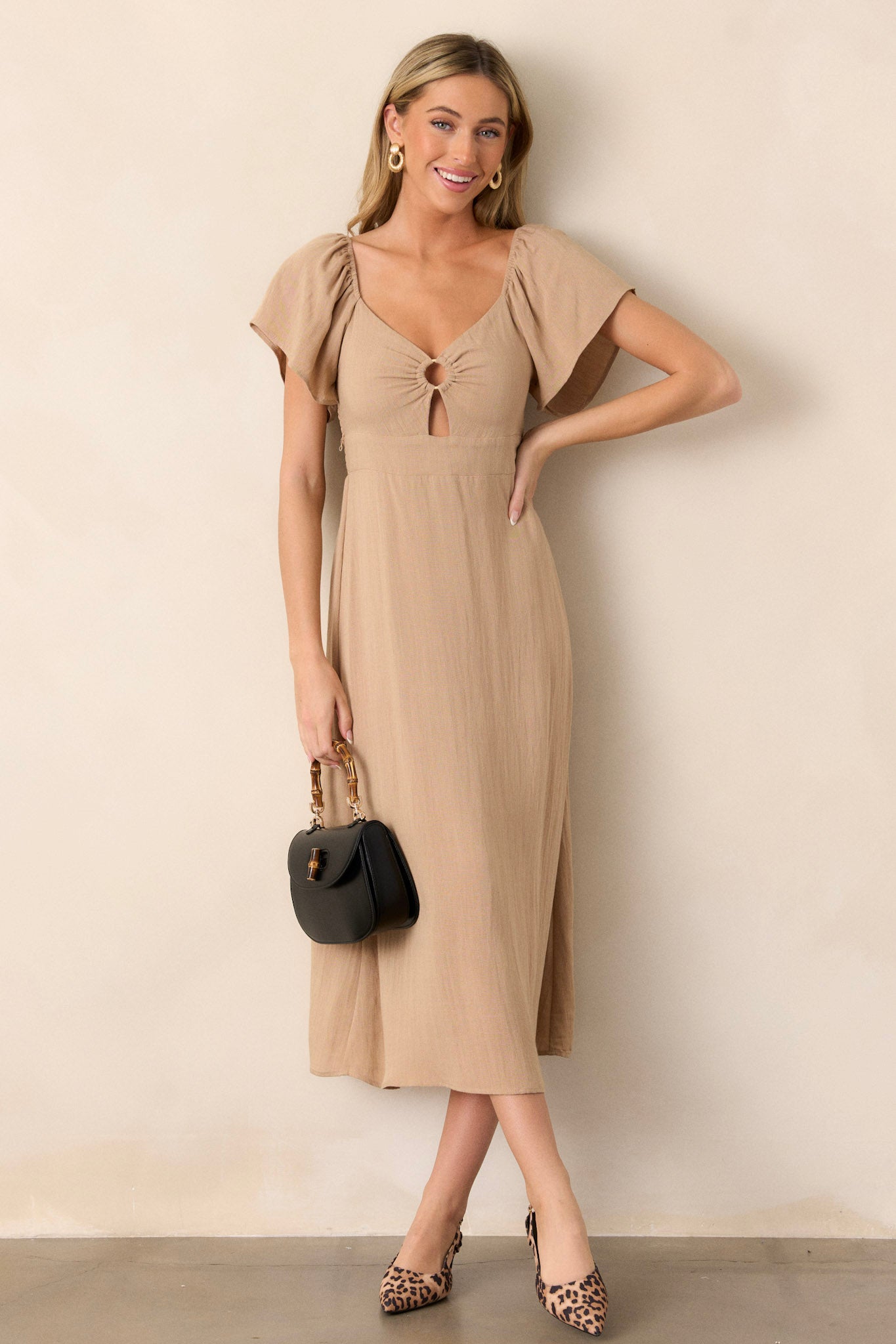 This midi dress features a cut-out design in the chest, a smocked back, elastic cuffed puff sleeves, an accent gold ring in the bust, and a flowing silhouette.