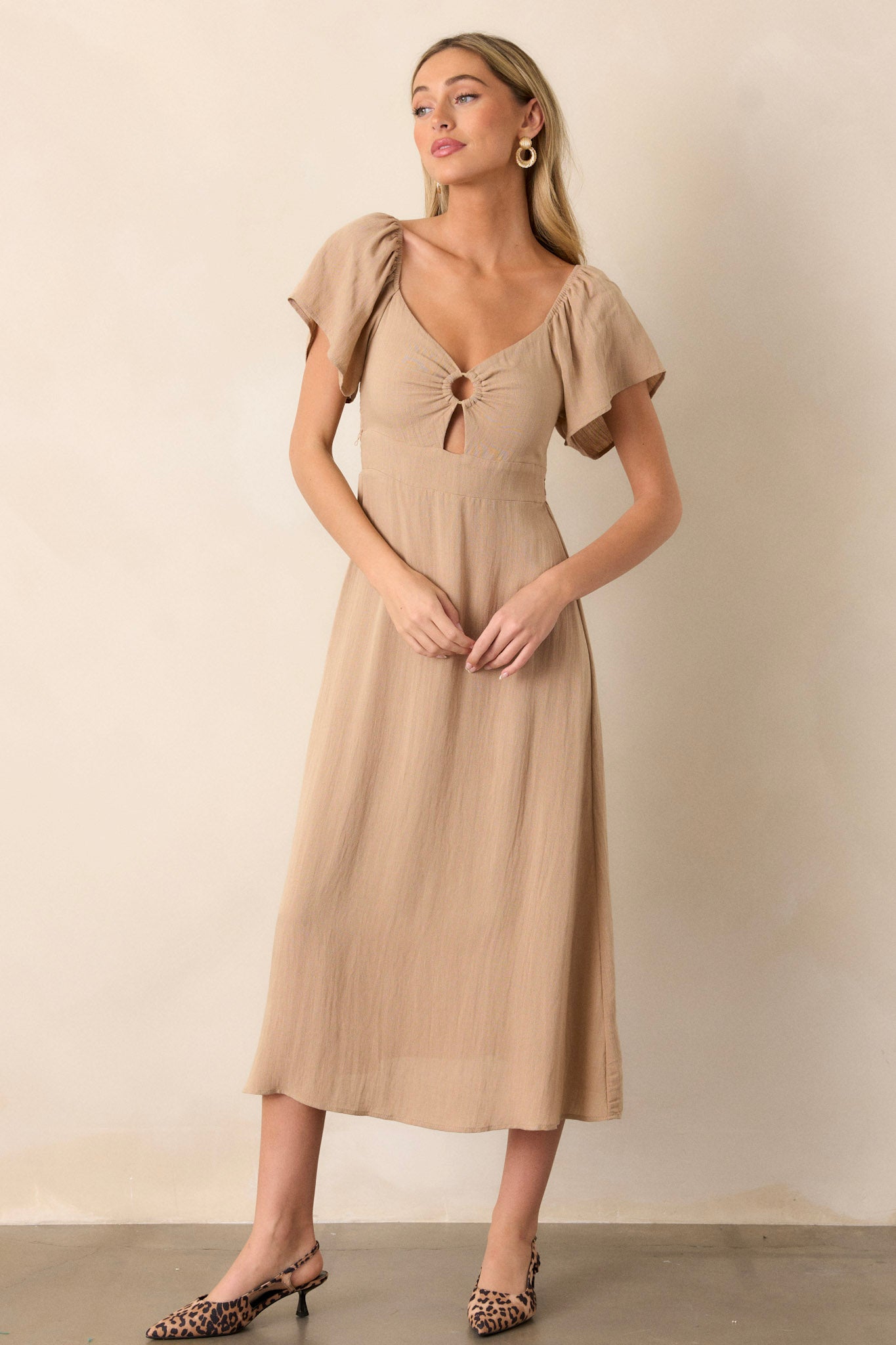 Action shot of a midi dress displaying the fit and movement, highlighting the cut-out design in the chest, smocked back, elastic cuffed puff sleeves, accent gold ring in the bust, and flowing silhouette.