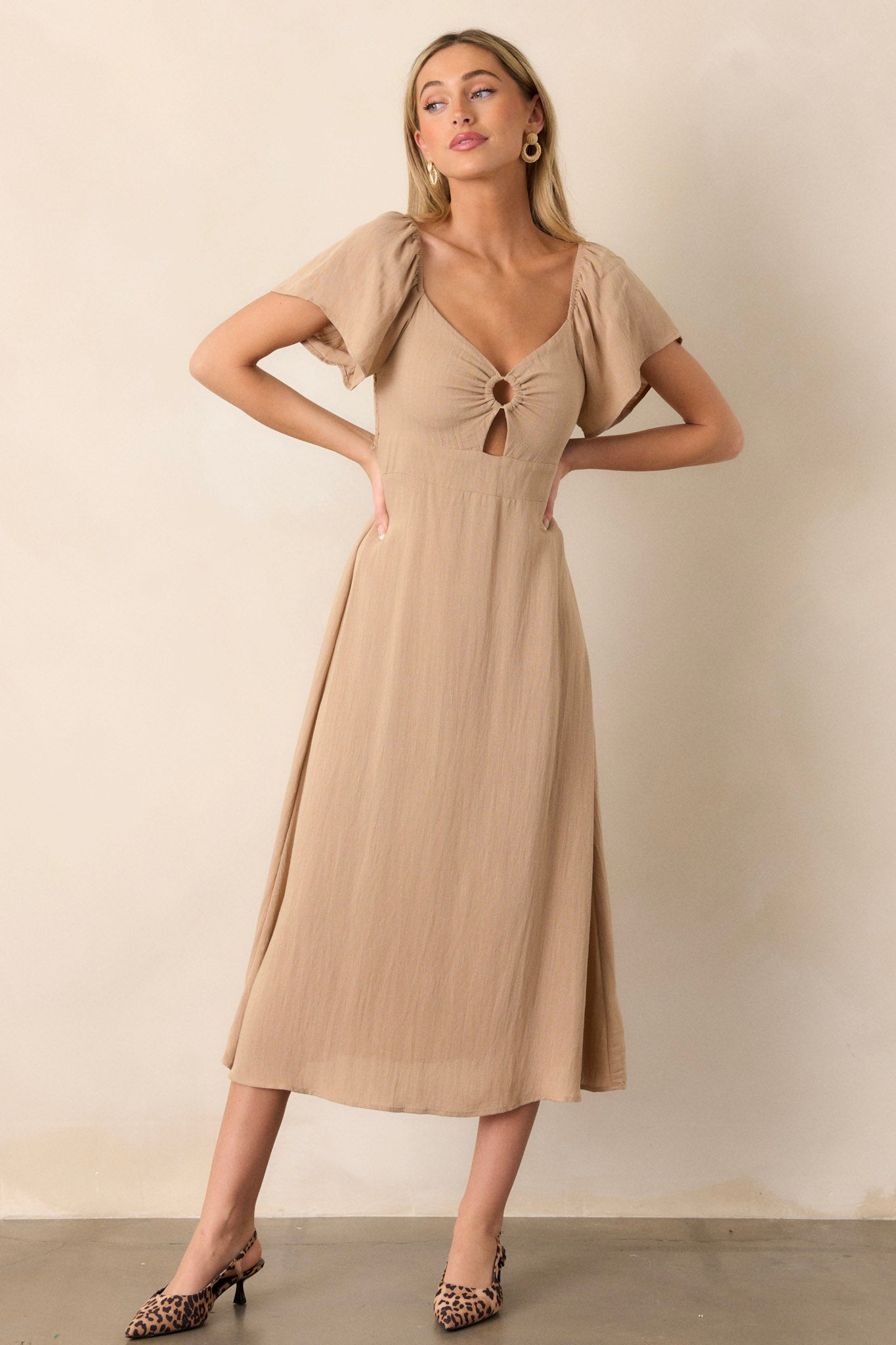 Front view of a midi dress featuring a cut-out design in the chest, a smocked back, elastic cuffed puff sleeves, an accent gold ring in the bust, and a flowing silhouette.