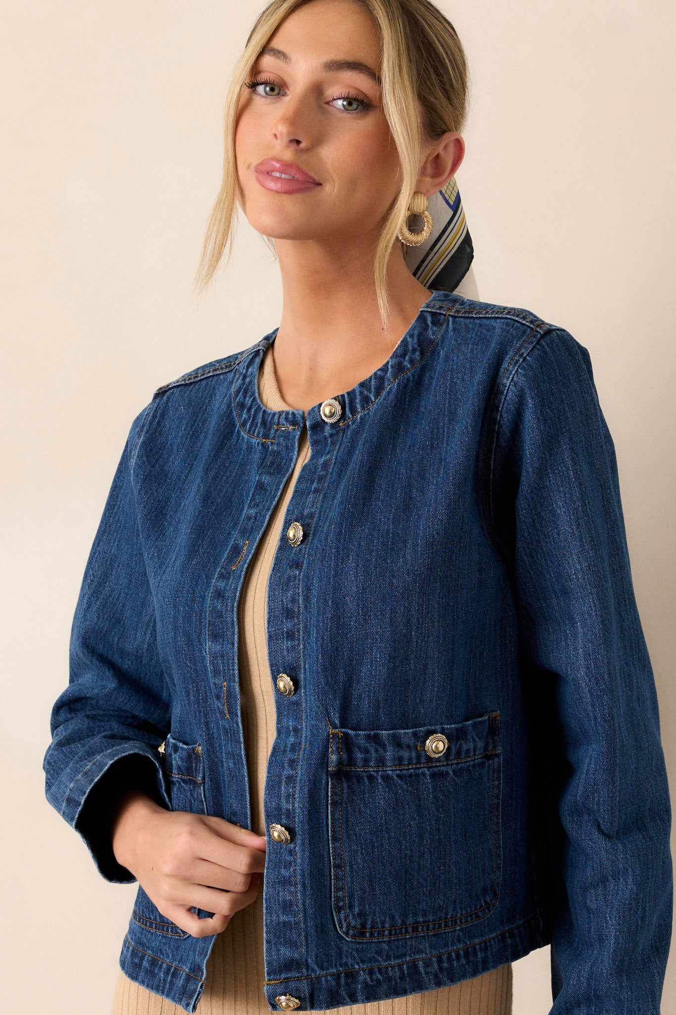 This dark denim jacket features a rounded neckline, a functional button front, gold accent buttons, functional front pockets, and long sleeves.