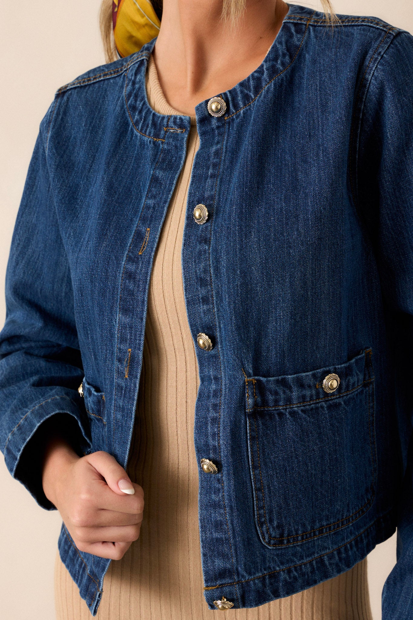 Close-up of the dark denim jacket focusing on the rounded neckline, functional button front with gold accent buttons, and one of the functional front pockets.